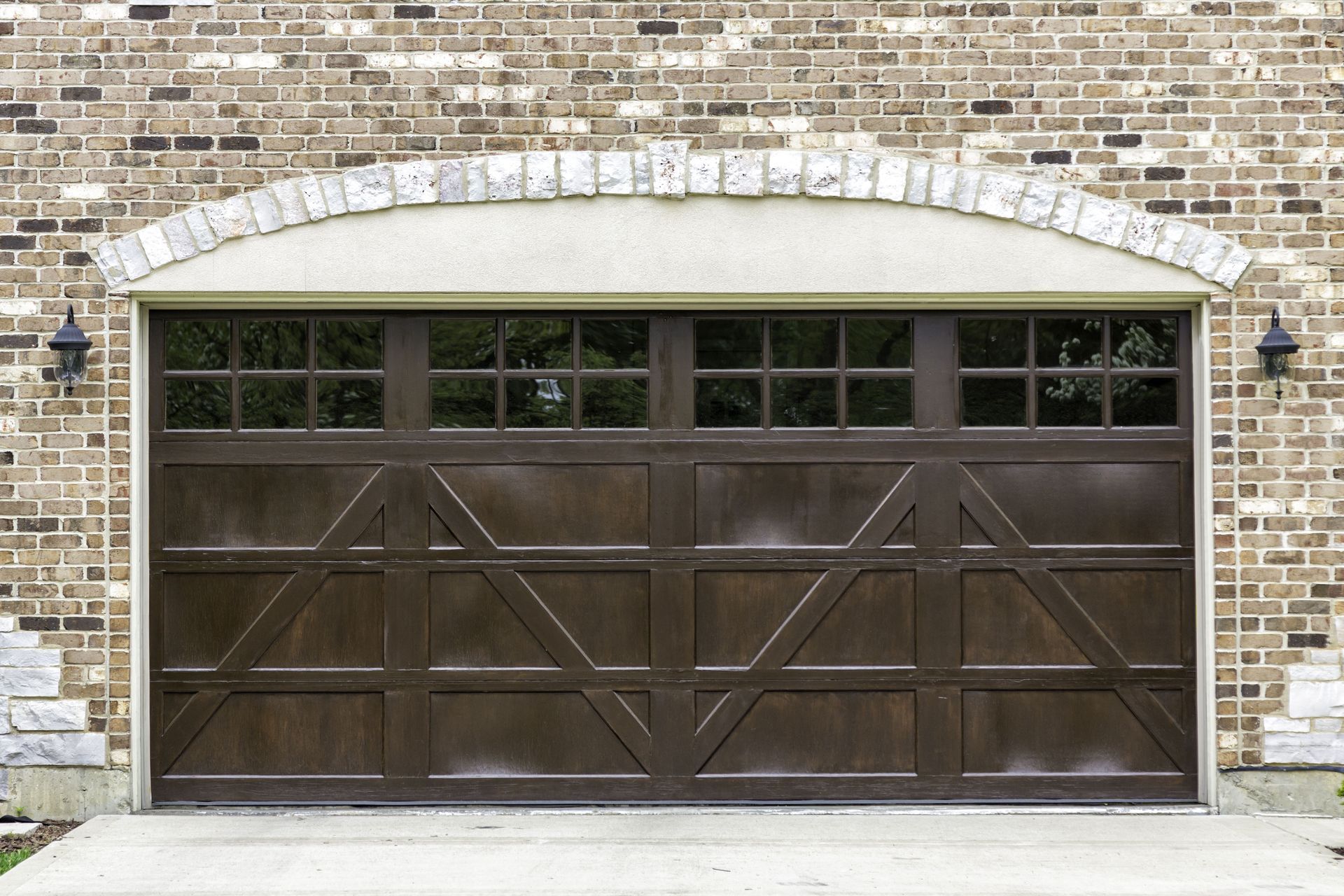 Brown garage door with glass panels above, set in brick wall.