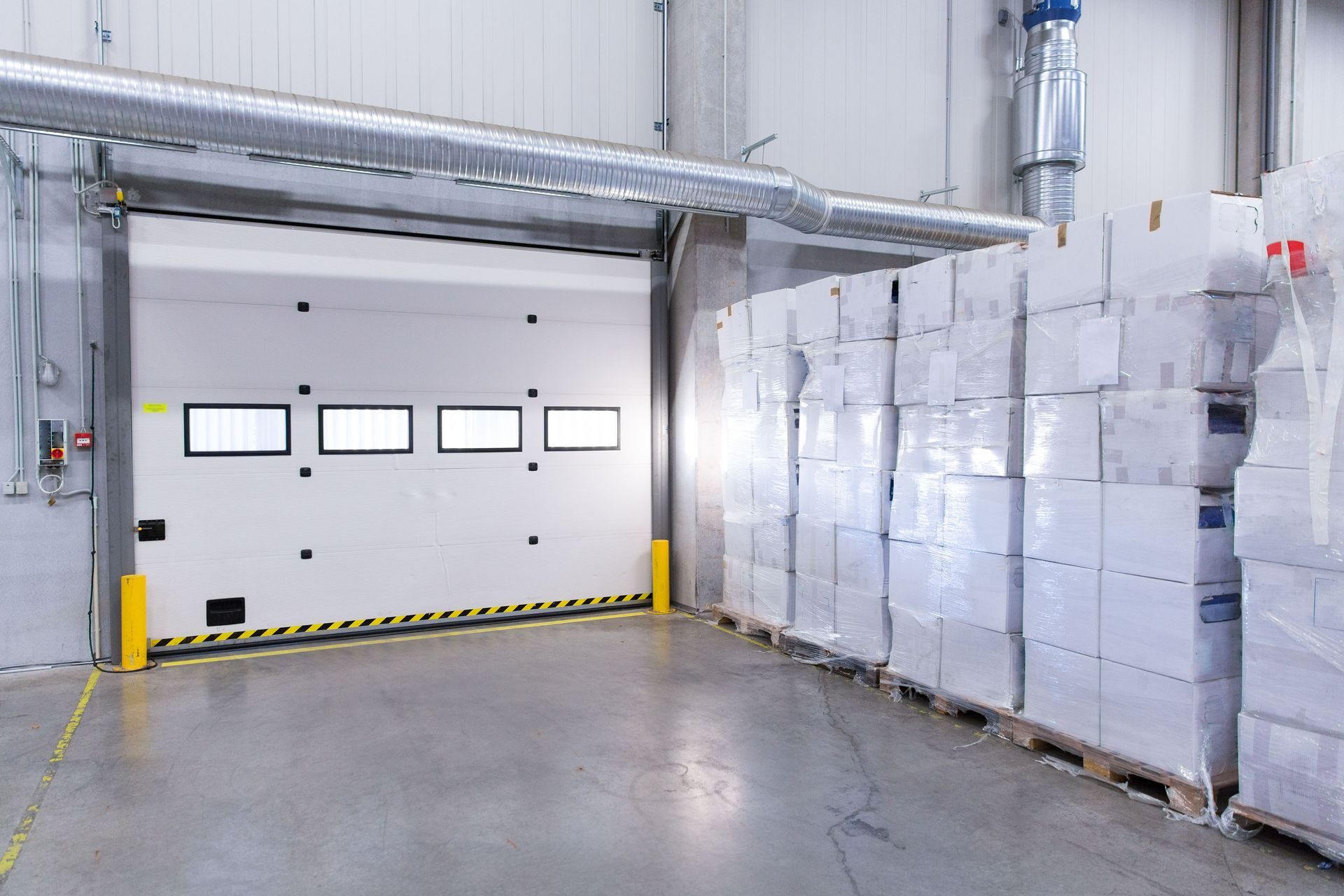 Warehouse loading dock door open with stacks of wrapped boxes on pallets.