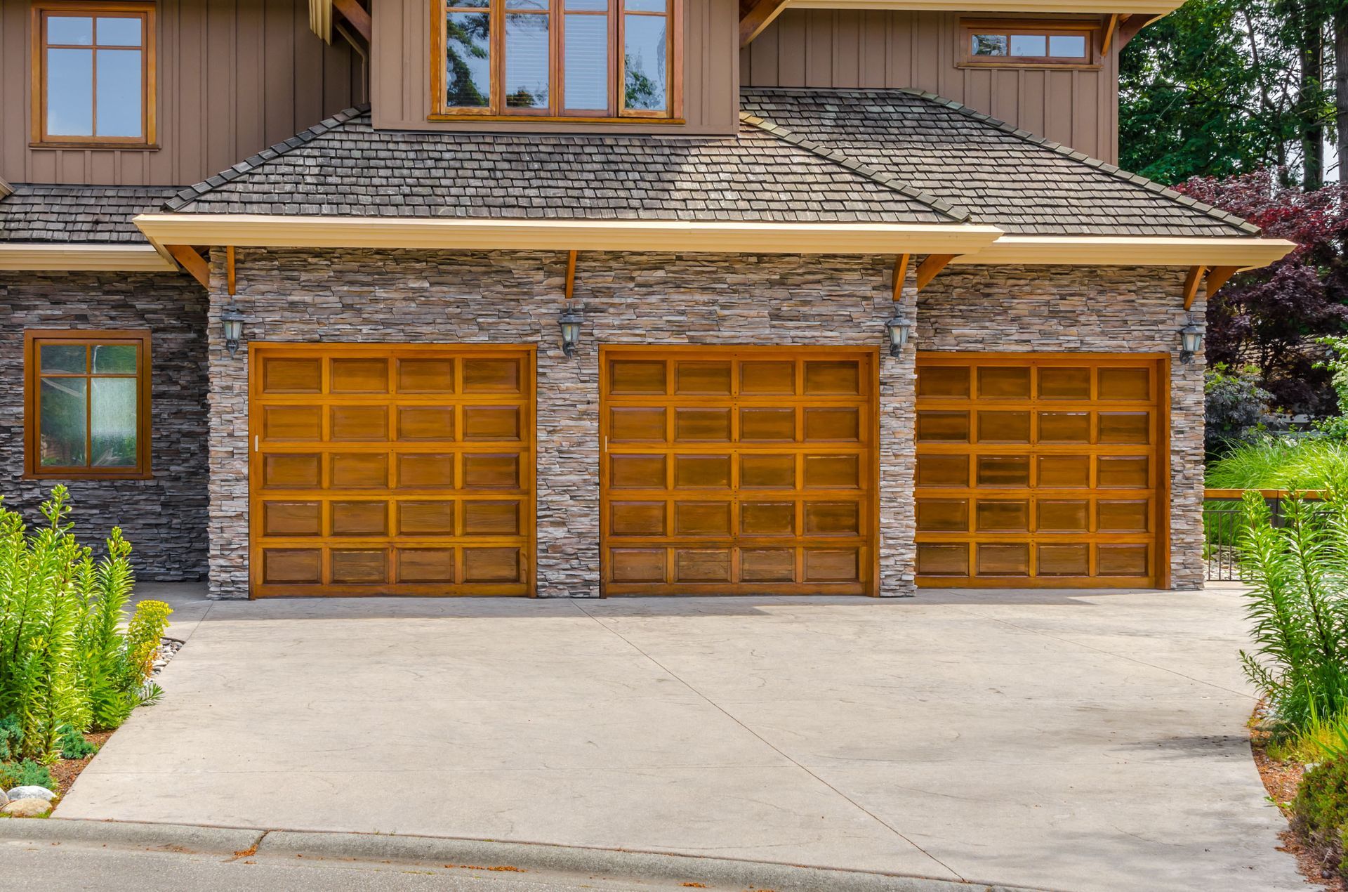 Three car garage with brown doors, stone facade, and concrete driveway.