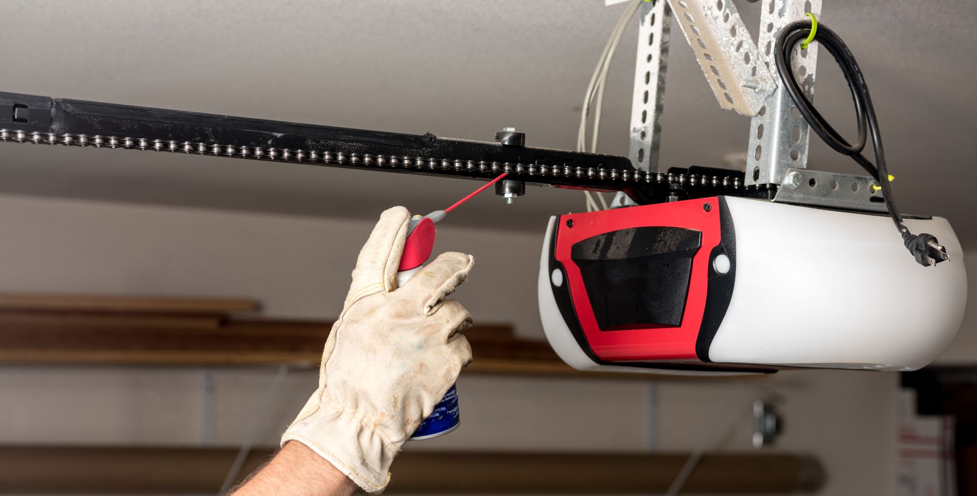 Person in glove lubricates garage door opener chain with spray can.