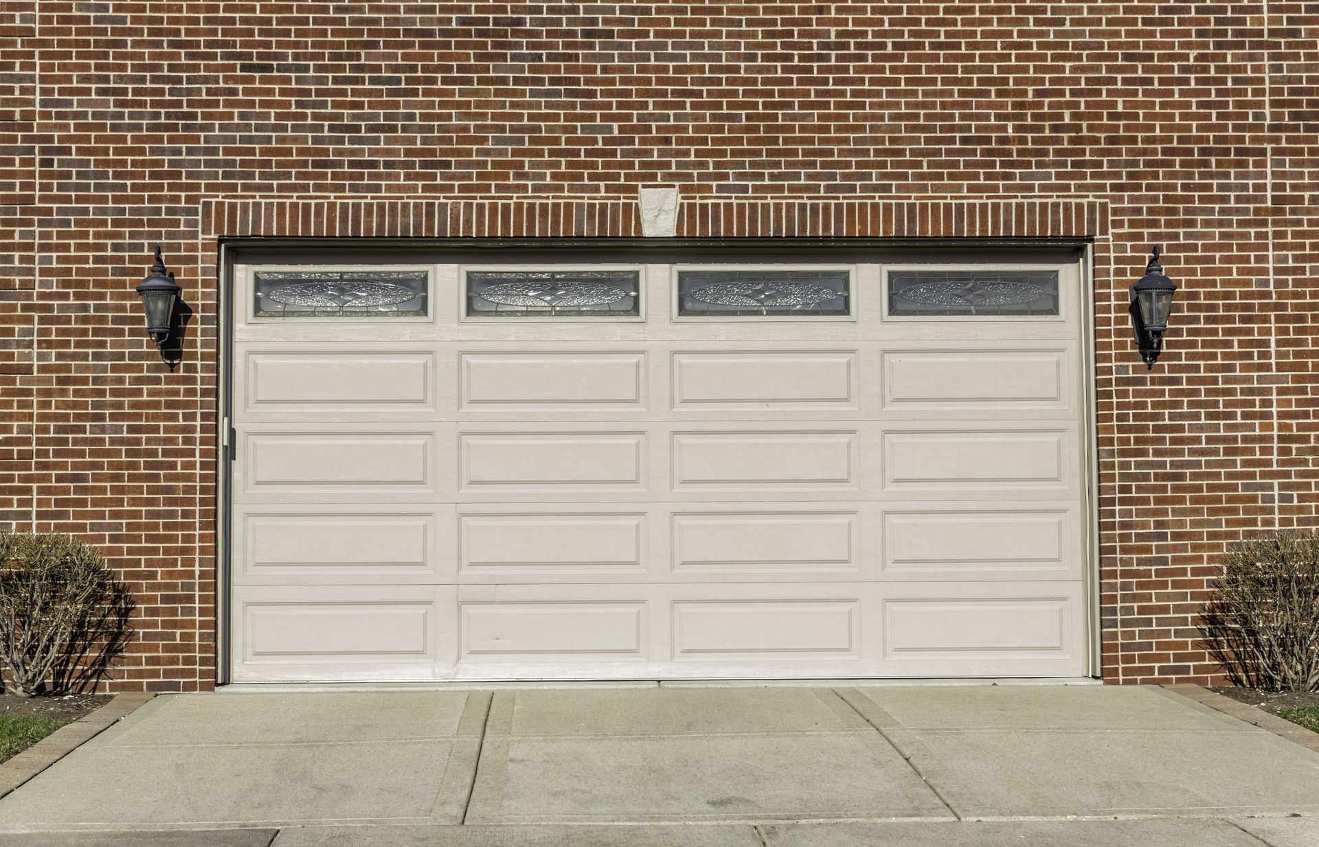 Tan garage door on a brick building with a concrete driveway.