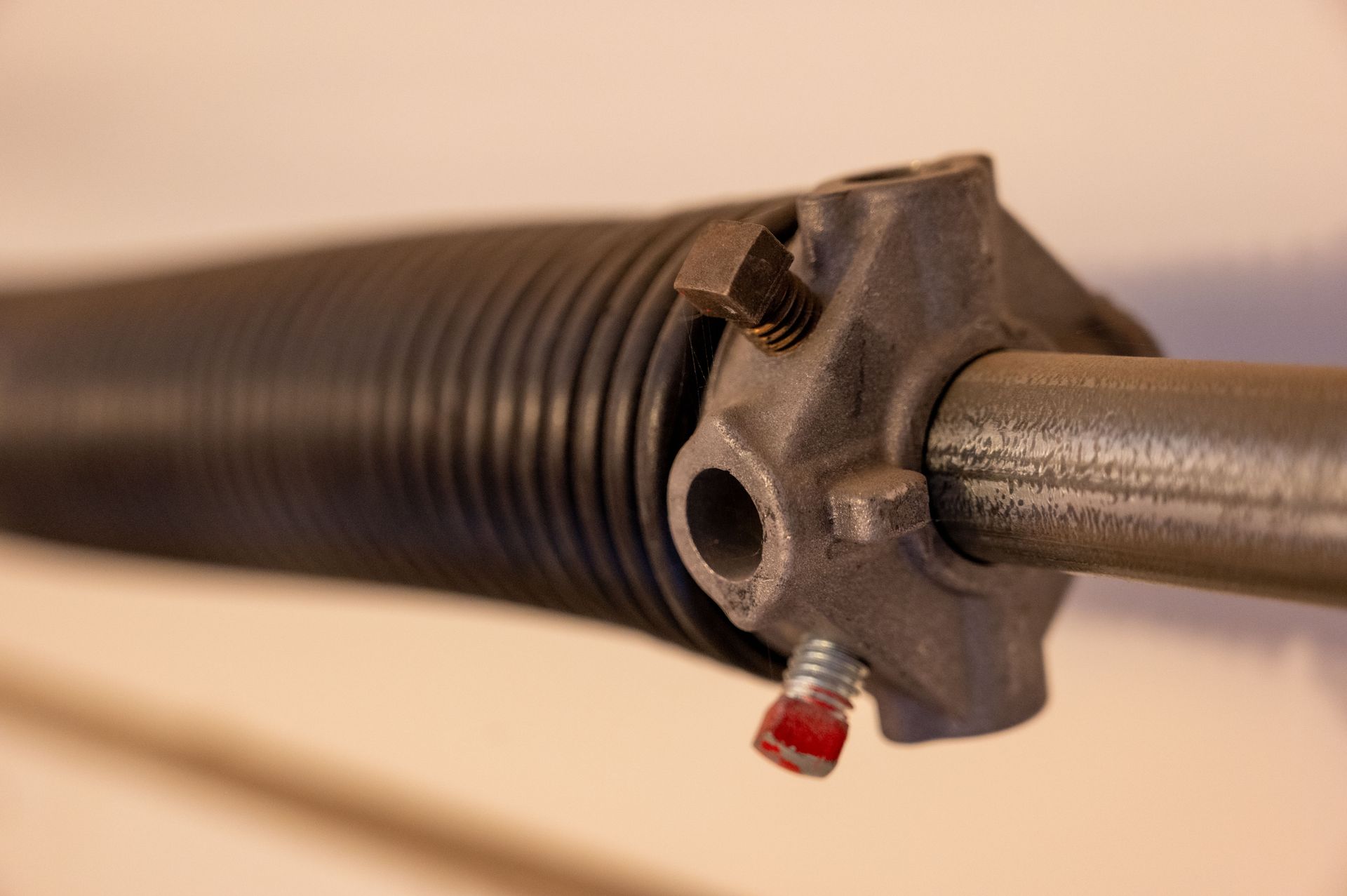 Close-up of a garage door spring system; black coil spring, metal rod, and grey metal mounts.