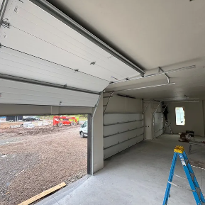 Two white garage doors on a gray house with a concrete driveway.