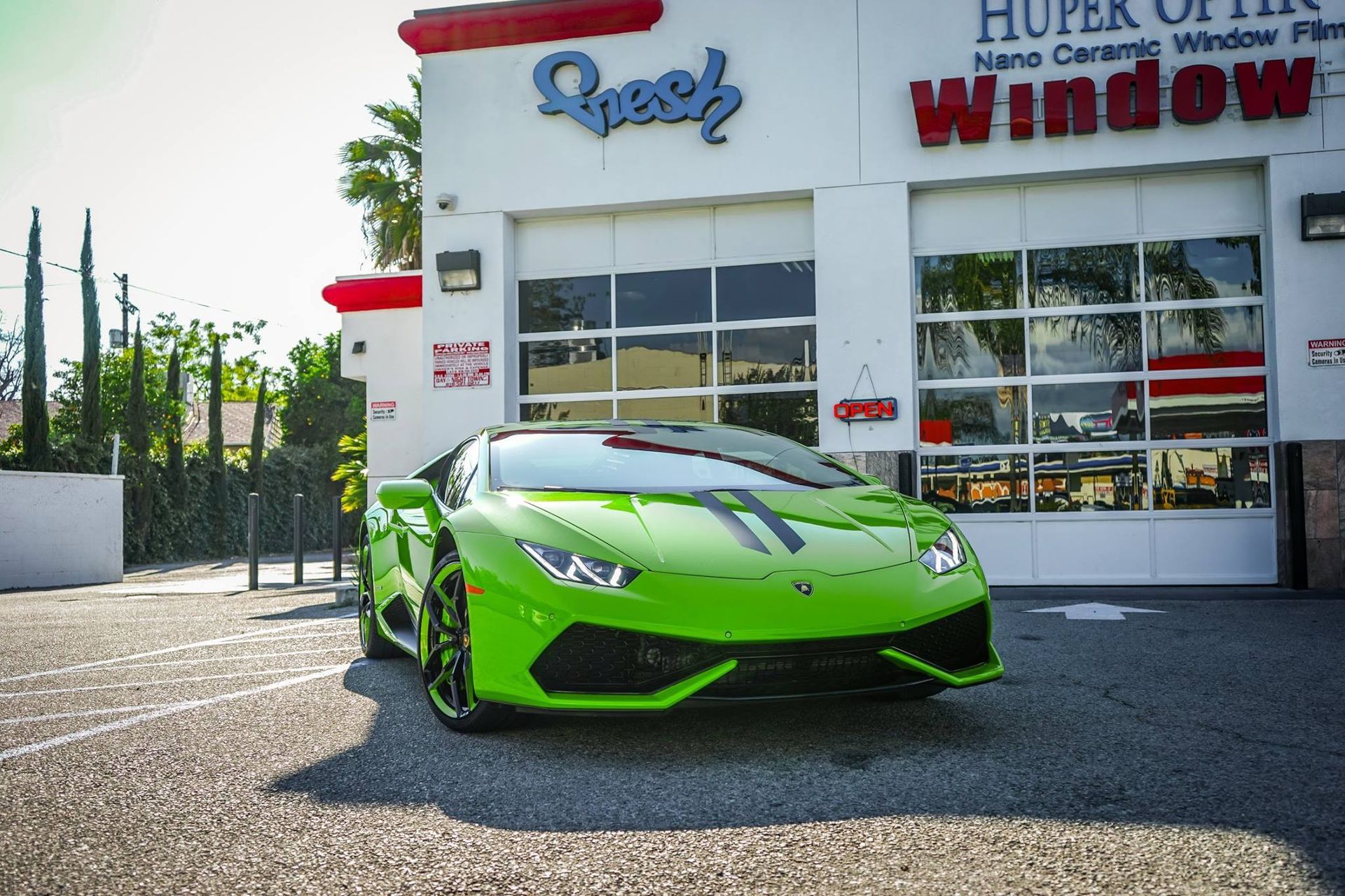 Green Lamborghini parked outside a window tinting business with garage doors and text signage.