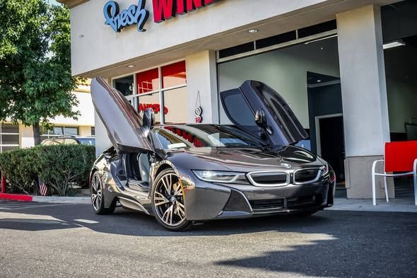 Dark gray BMW i8 with doors open, parked in front of a car wash.