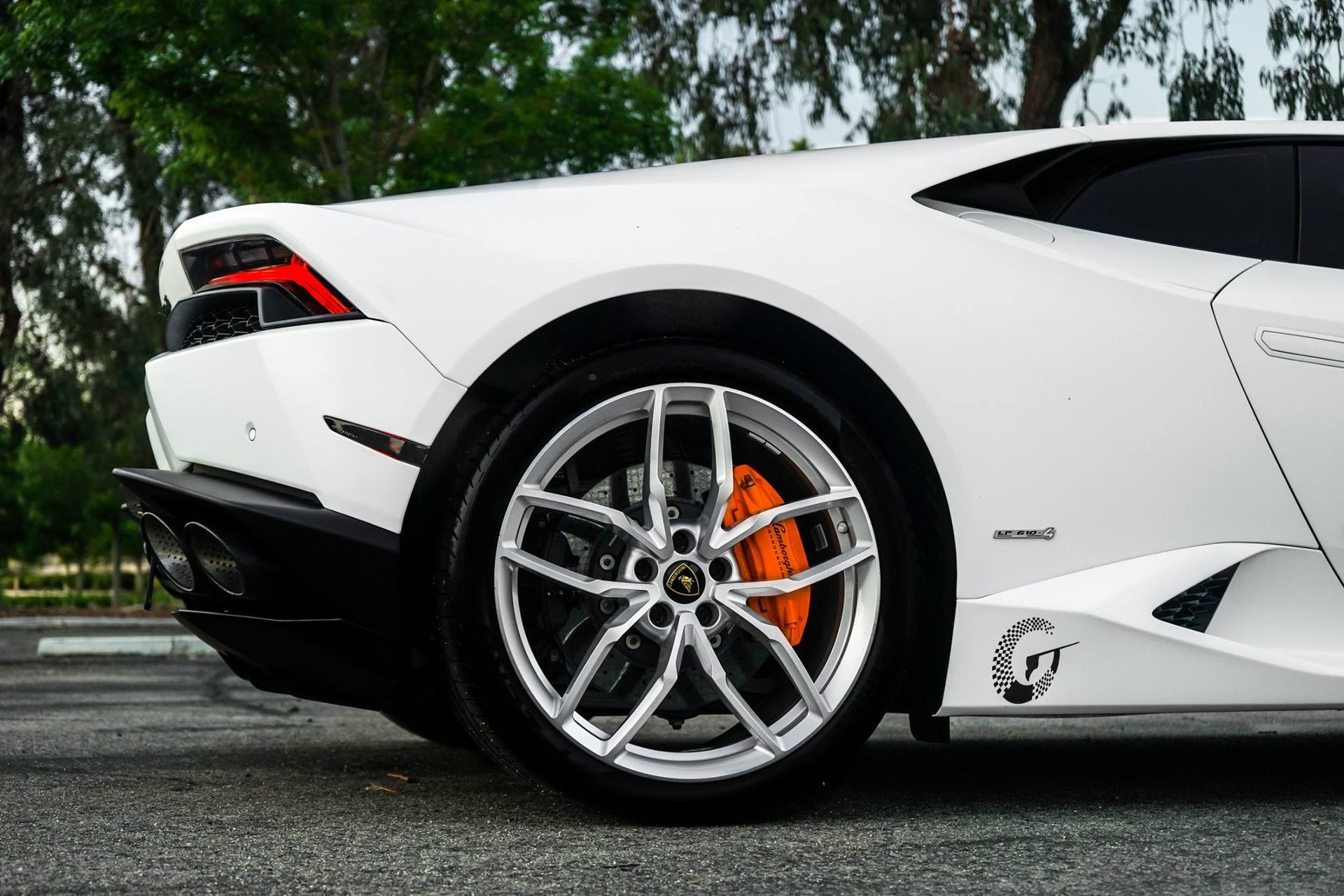 White Lamborghini sports car, rear quarter view, orange brake calipers, silver wheels.