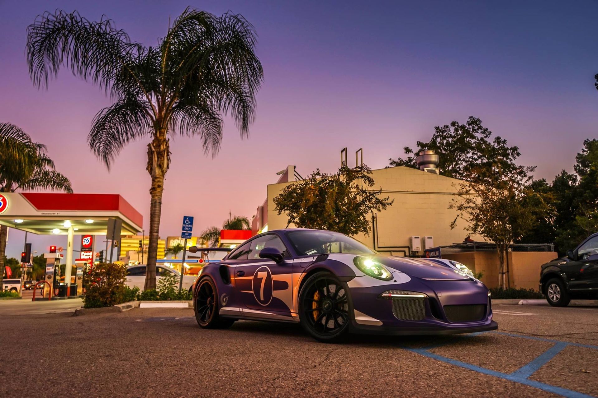 Purple Porsche sports car parked at a gas station under a twilight sky.