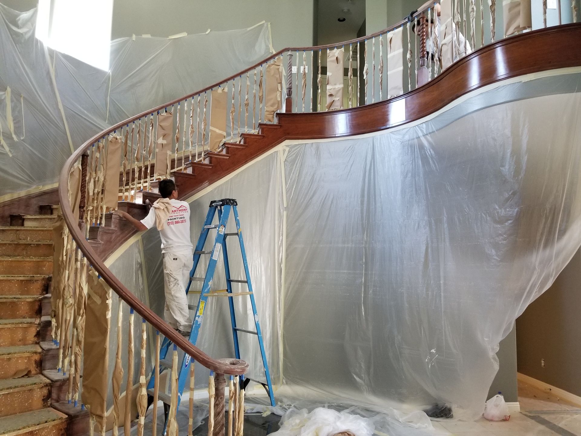 A man is standing on a ladder painting a staircase.