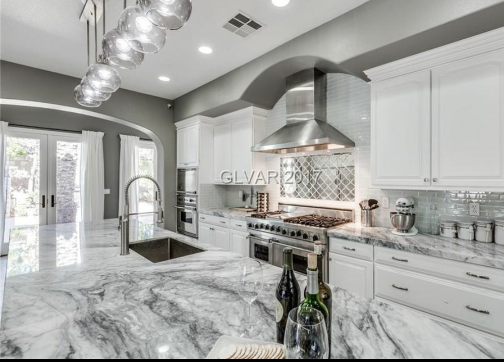 A kitchen with white cabinets and marble counter tops.