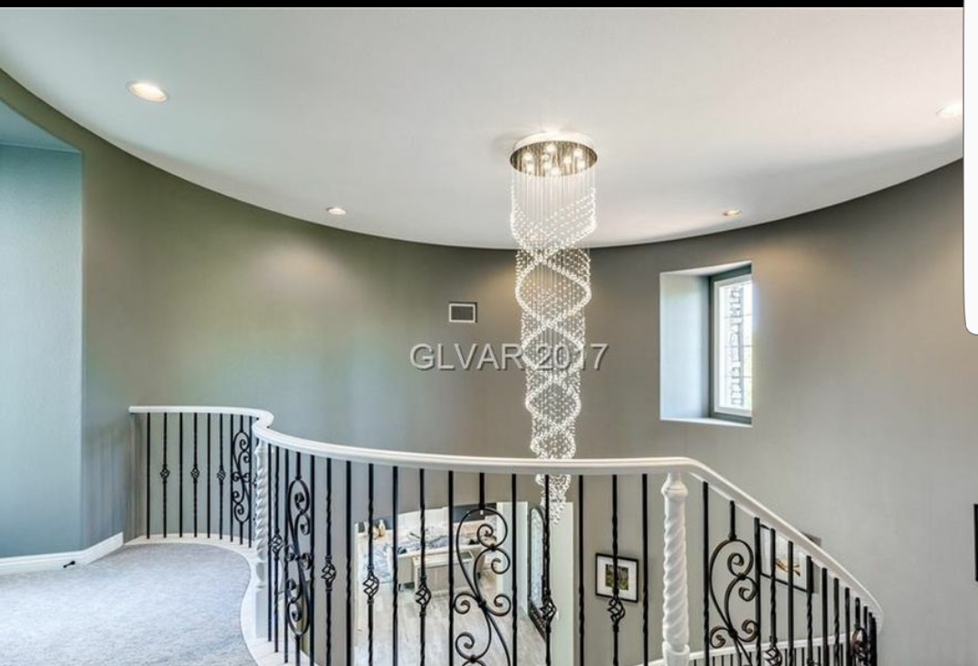 A curved staircase with a modern chandelier hanging from the ceiling. The walls are gray with a small window.
