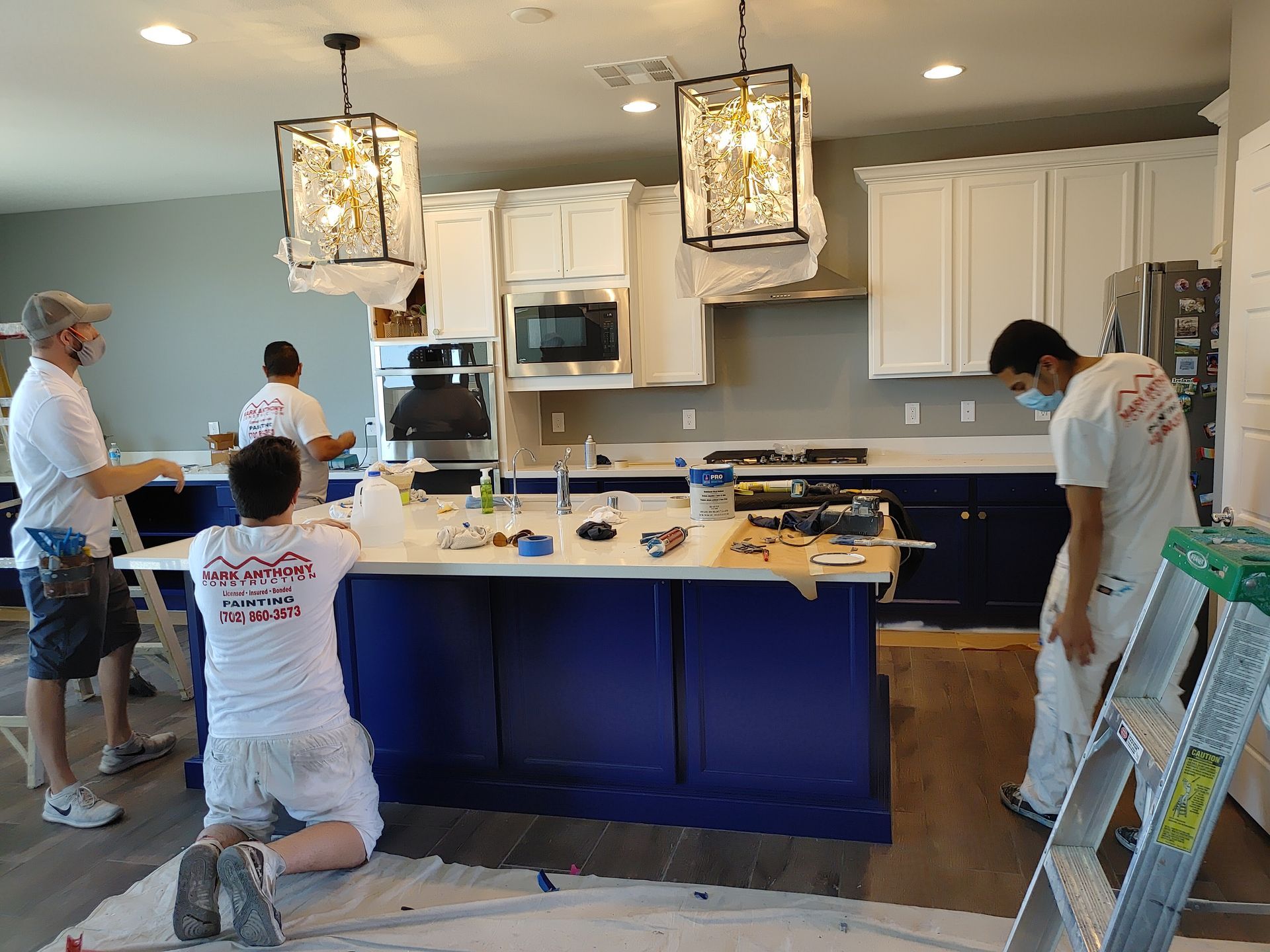 A group of men are painting a kitchen with blue cabinets and white cabinets.
