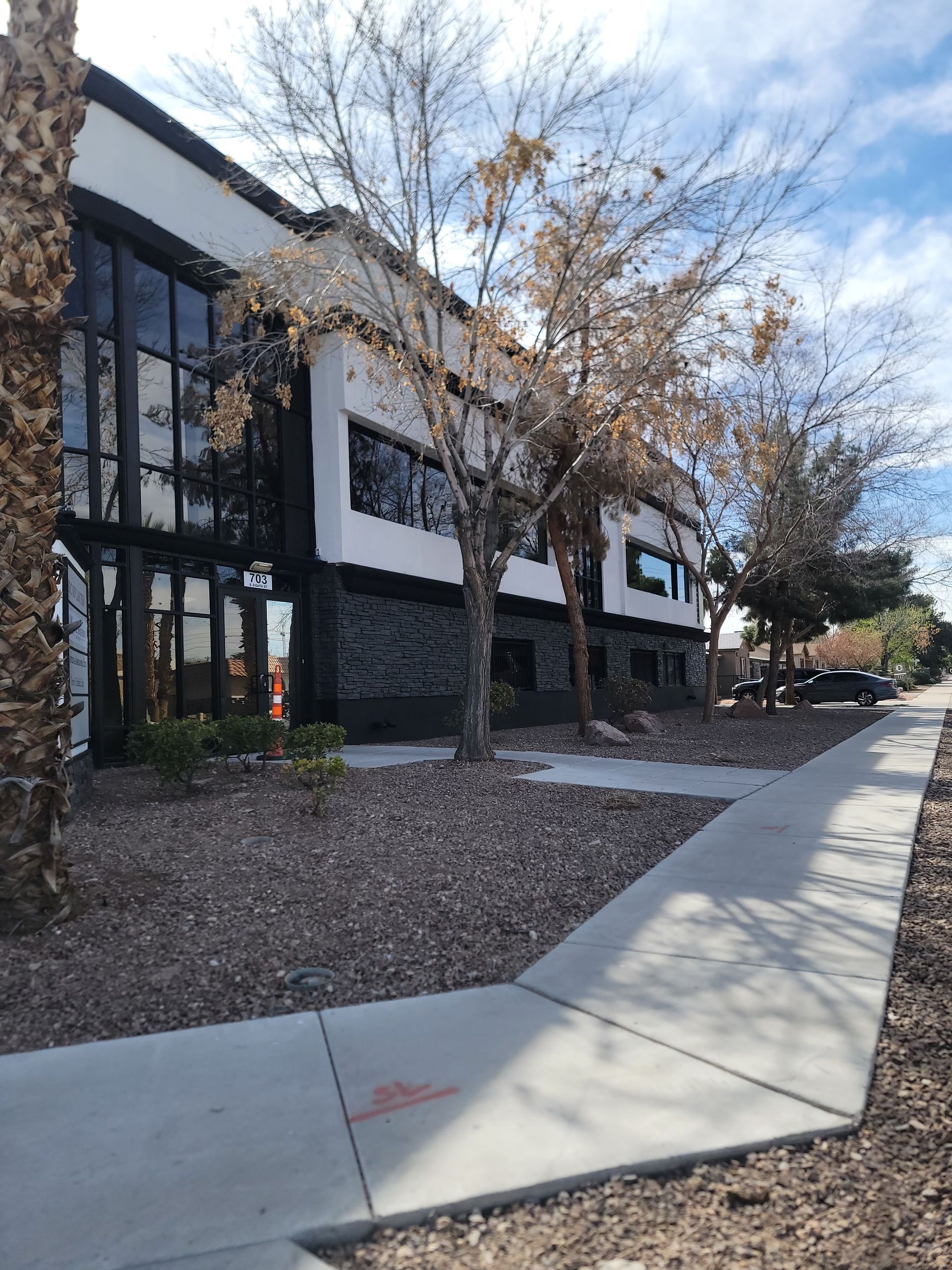 A sidewalk leading to a large building with trees in front of it.