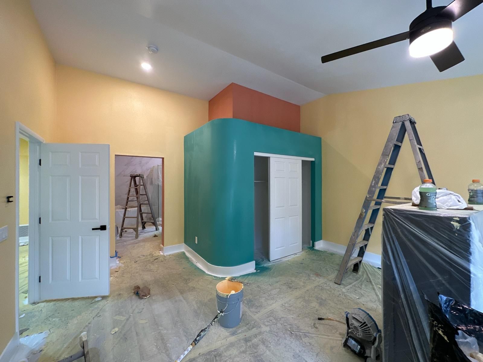 A room with a ceiling fan and a ladder in it is being painted.