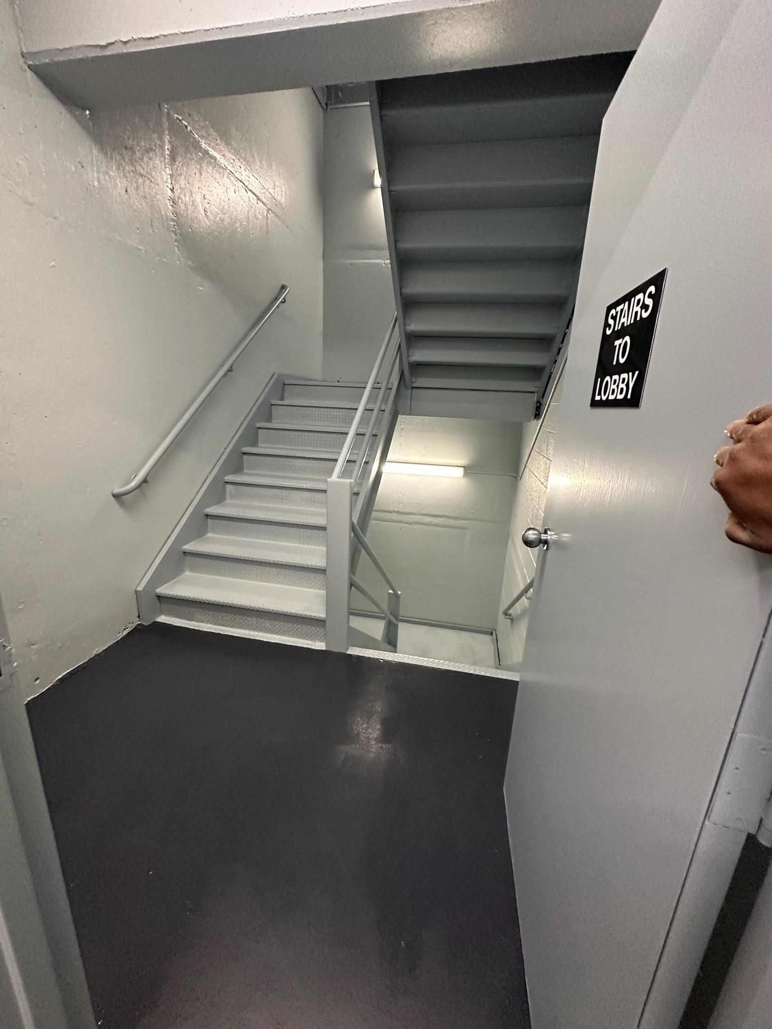 A person is standing in a hallway with stairs and a door.