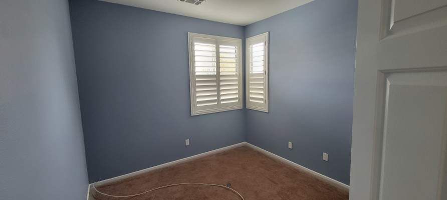 An empty room with blue walls and white shutters on the windows.