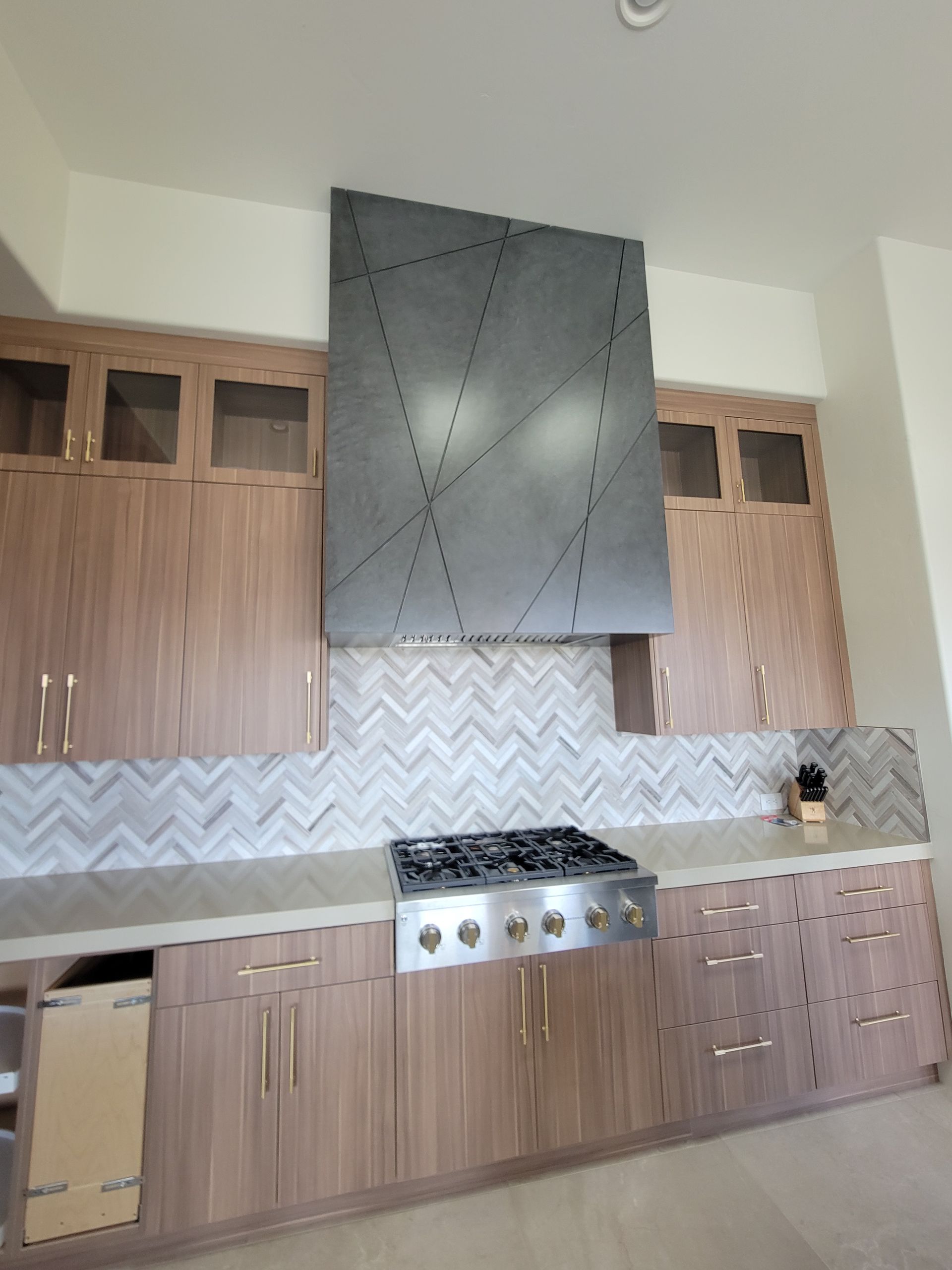 Kitchen with light wood cabinets, stainless steel range, geometric backsplash, and custom range hood.