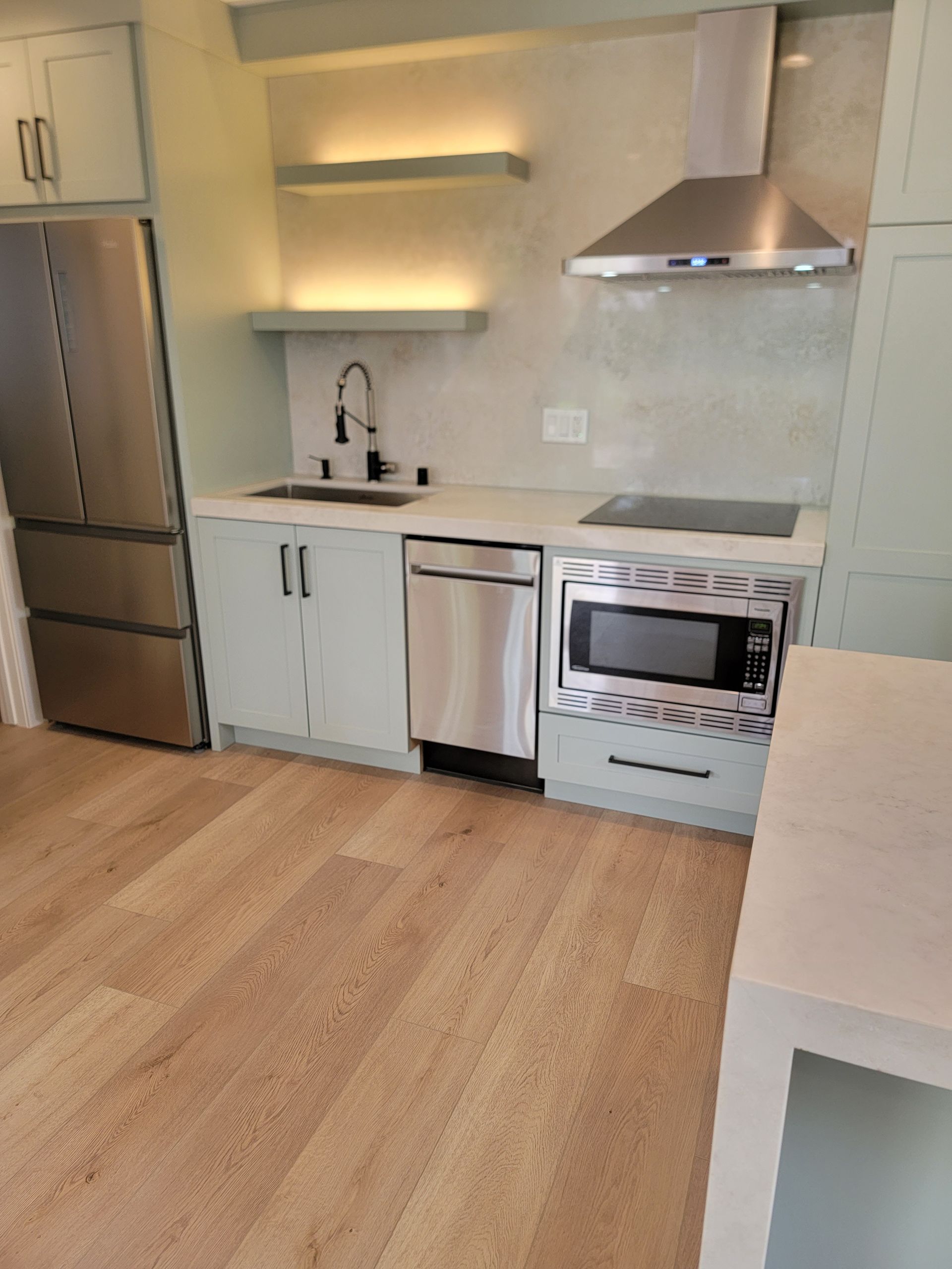 Small kitchen with stainless steel appliances, light blue cabinets, and light wood flooring.