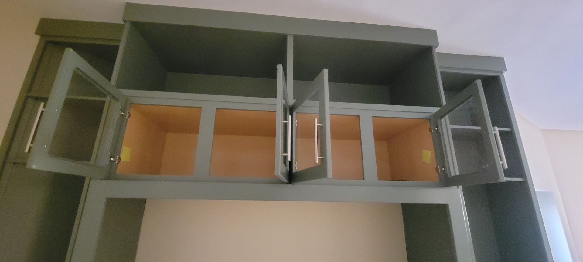 Open, empty, gray kitchen cabinets with glass doors. The interior is tan. The setting is indoors.