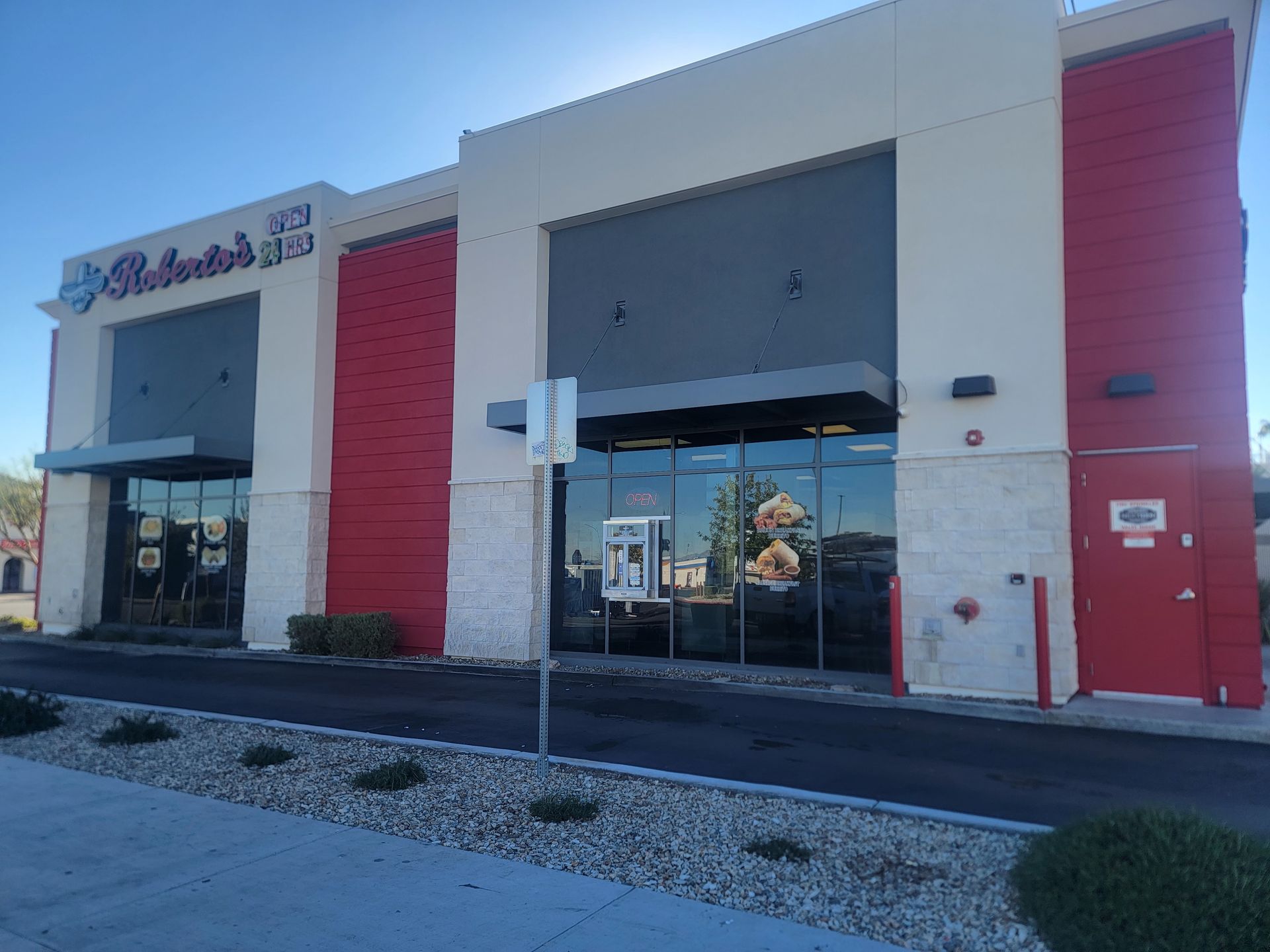 Exterior of Roberto's Taco Shop, beige and red building with large windows and a drive-thru lane, under a sunny sky.