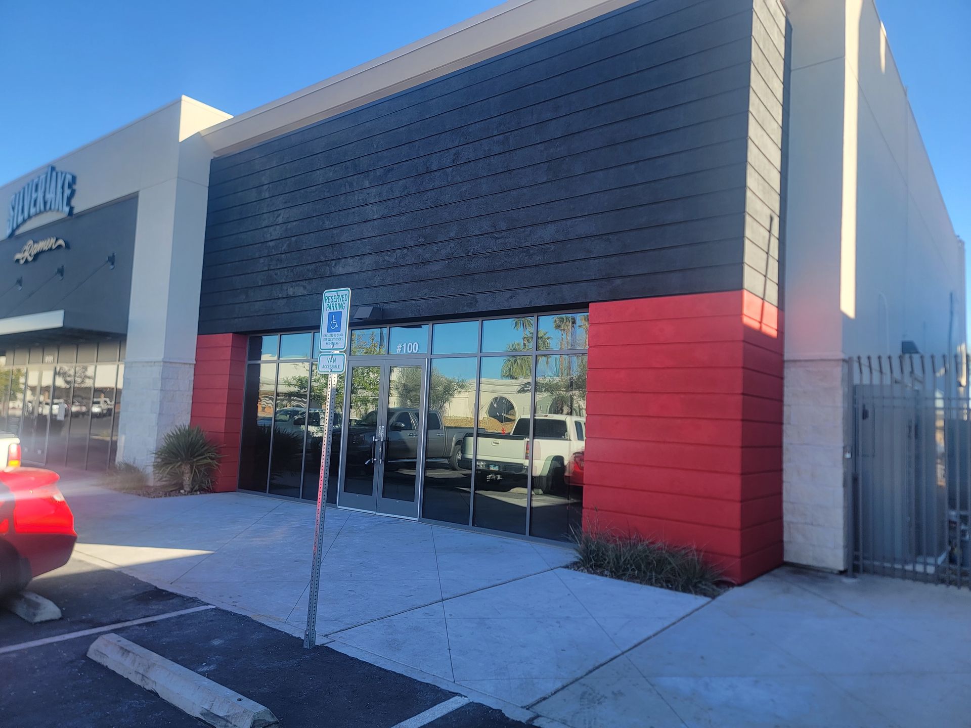 Exterior of a building with glass doors, red accents, and a blue handicap parking sign.