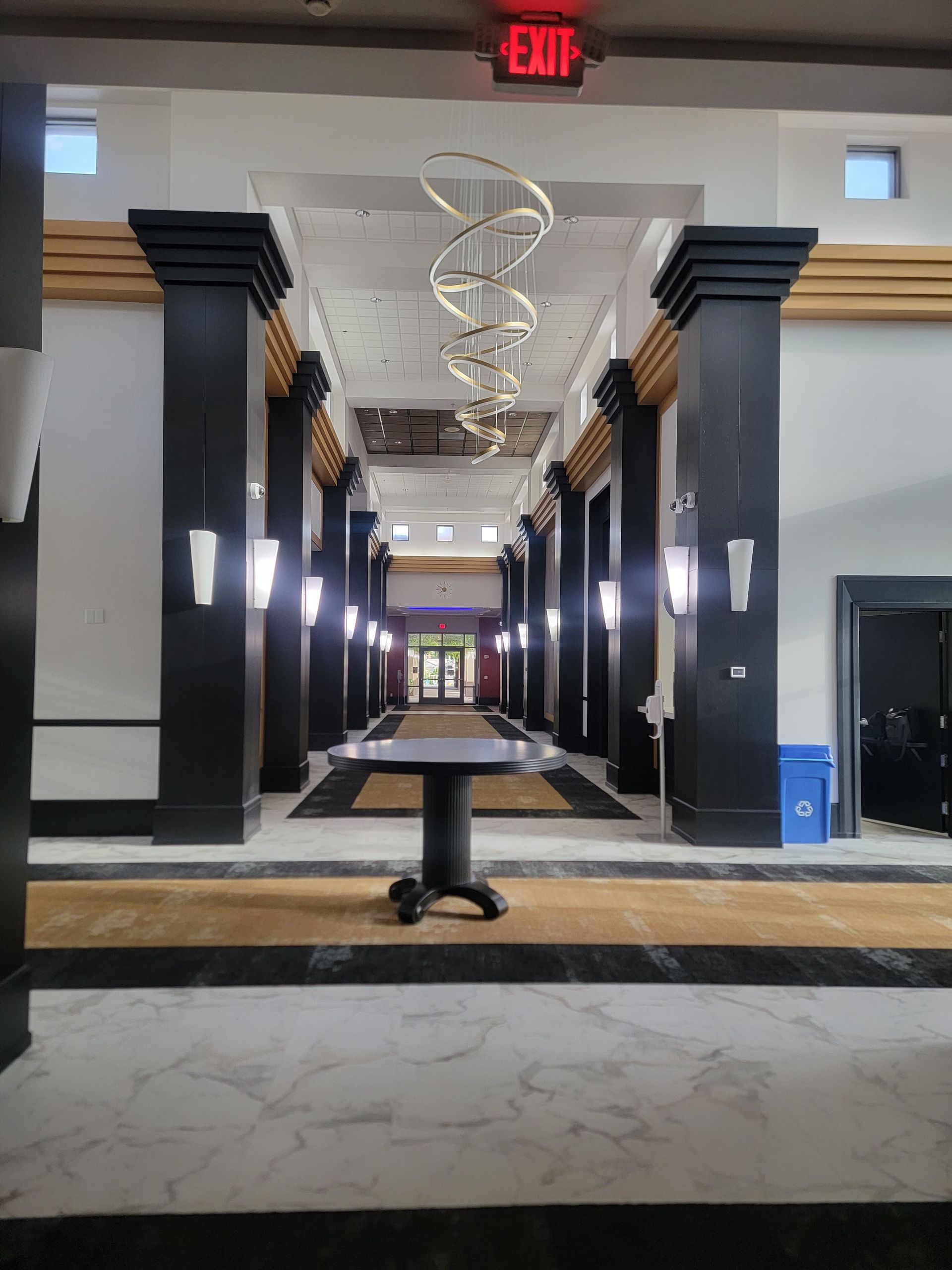 Hallway with black columns, gold accents, and a long table. White and gray floor.