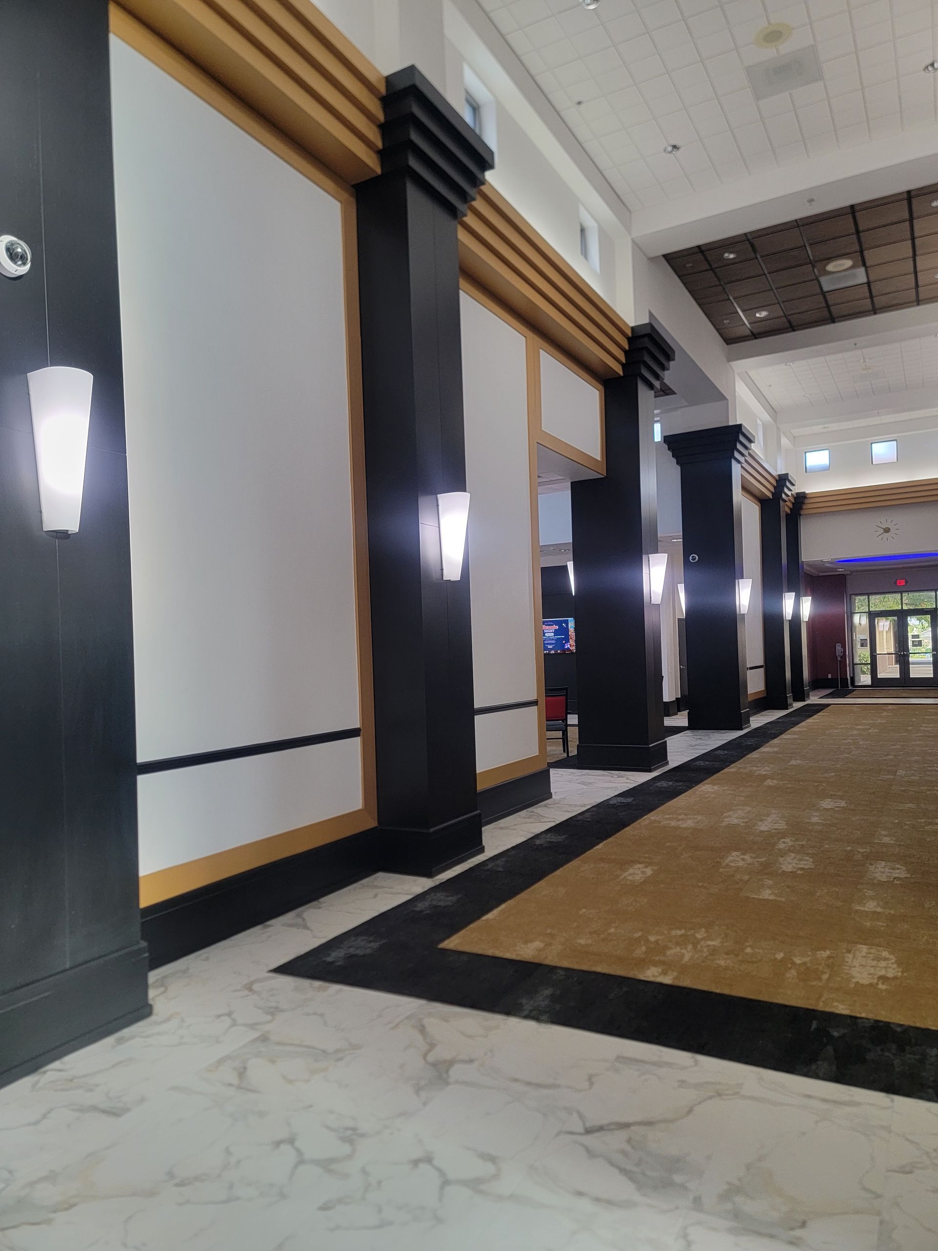 Interior hallway with black and gold pillars, white walls, and a patterned rug.