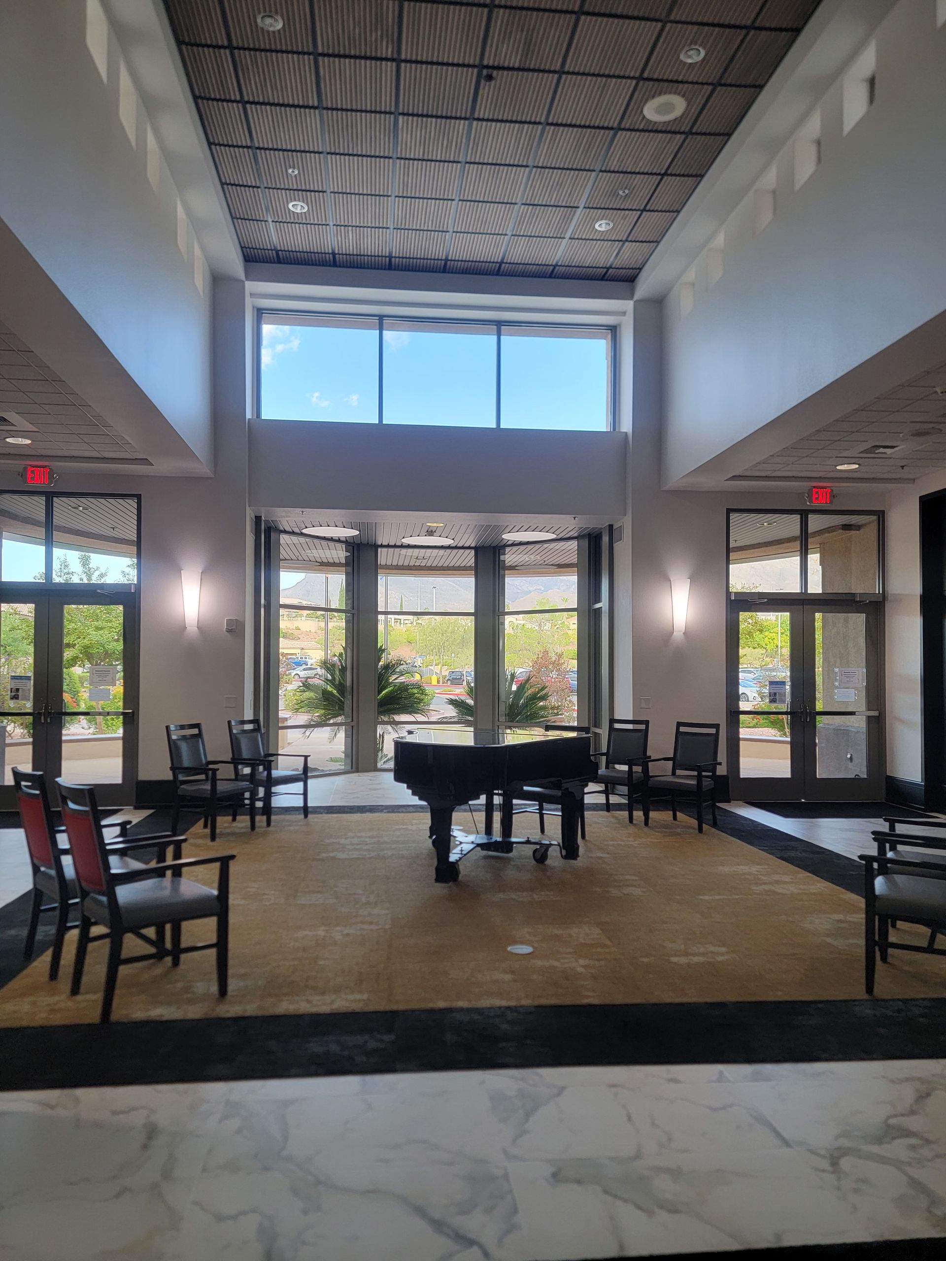 Spacious lobby with piano, chairs, and large windows looking outside. Neutral tones, good lighting.