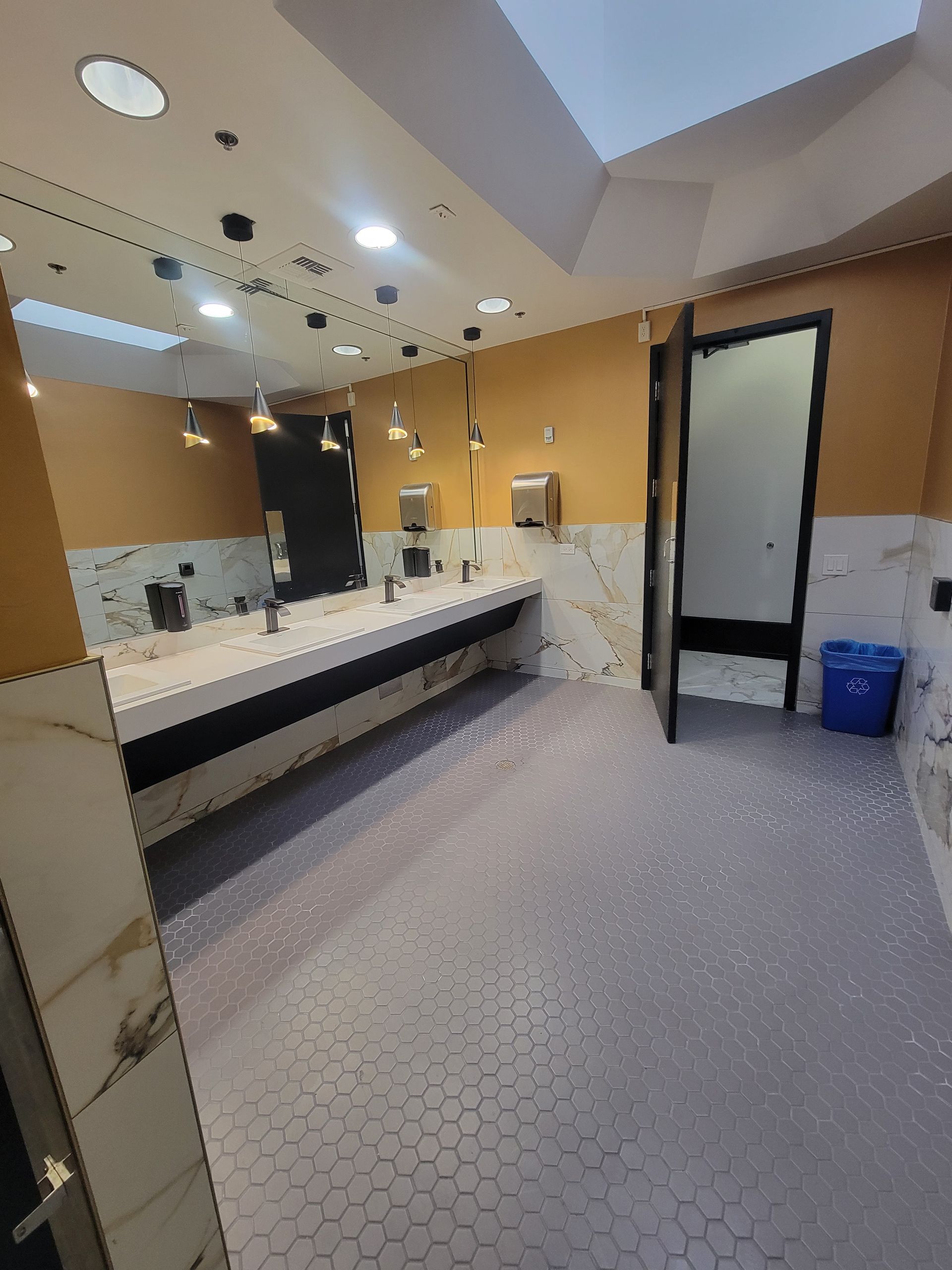 Public restroom with white sinks, yellow walls, gray hexagon tile floor, and an open door.