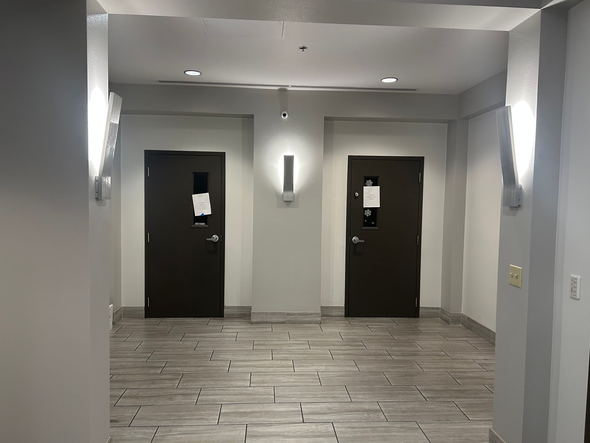 Hallway with two dark doors, bright lights, and tile flooring.
