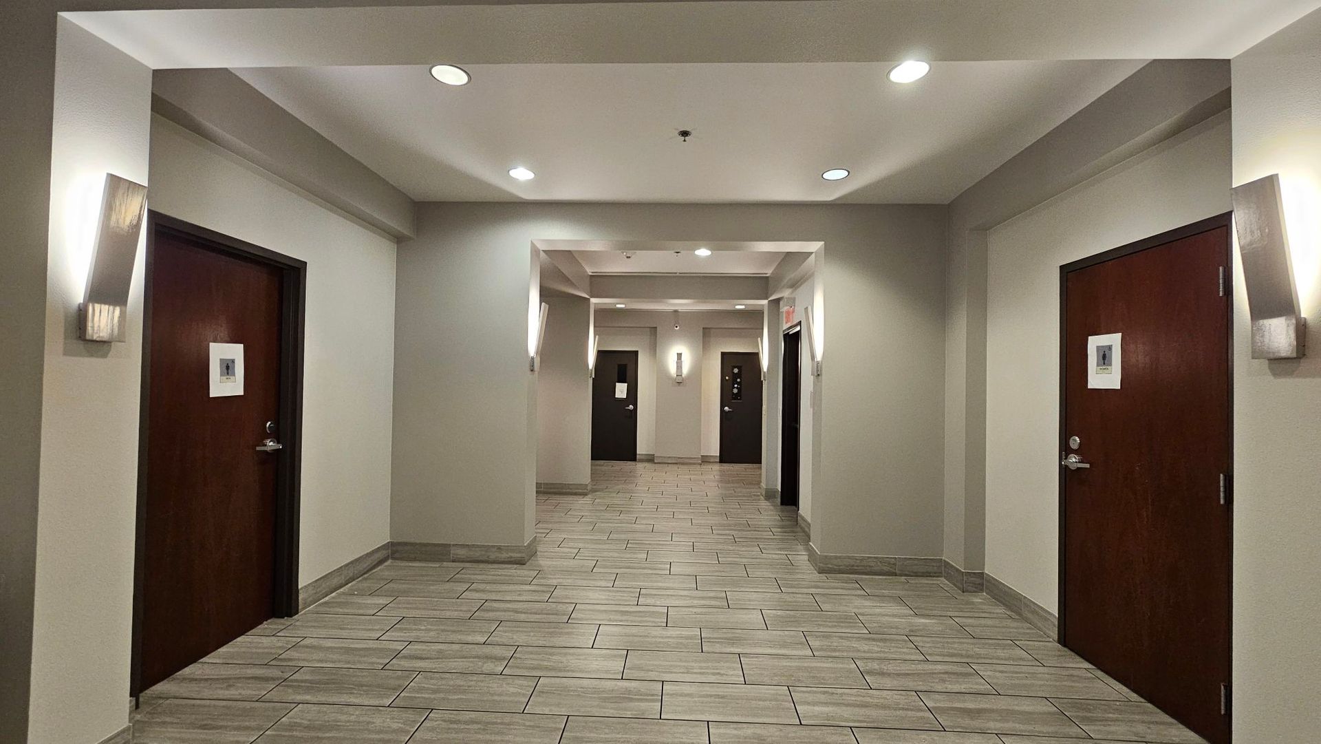 Hallway with wooden doors, sconce lighting, and tiled floor.