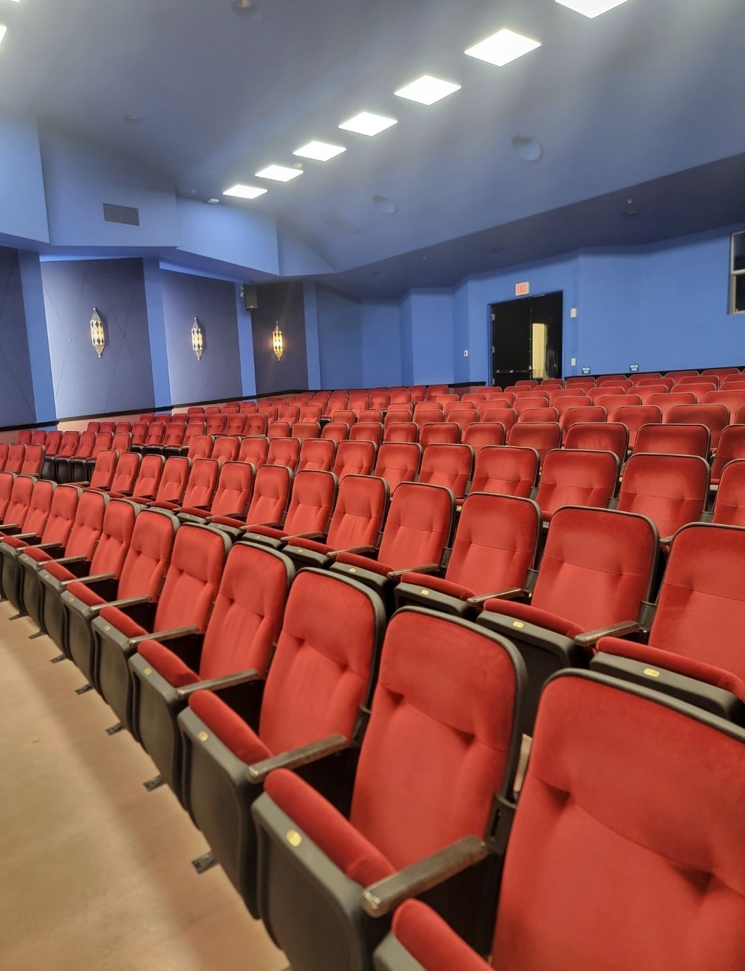 Empty theater with rows of red seats and blue walls.