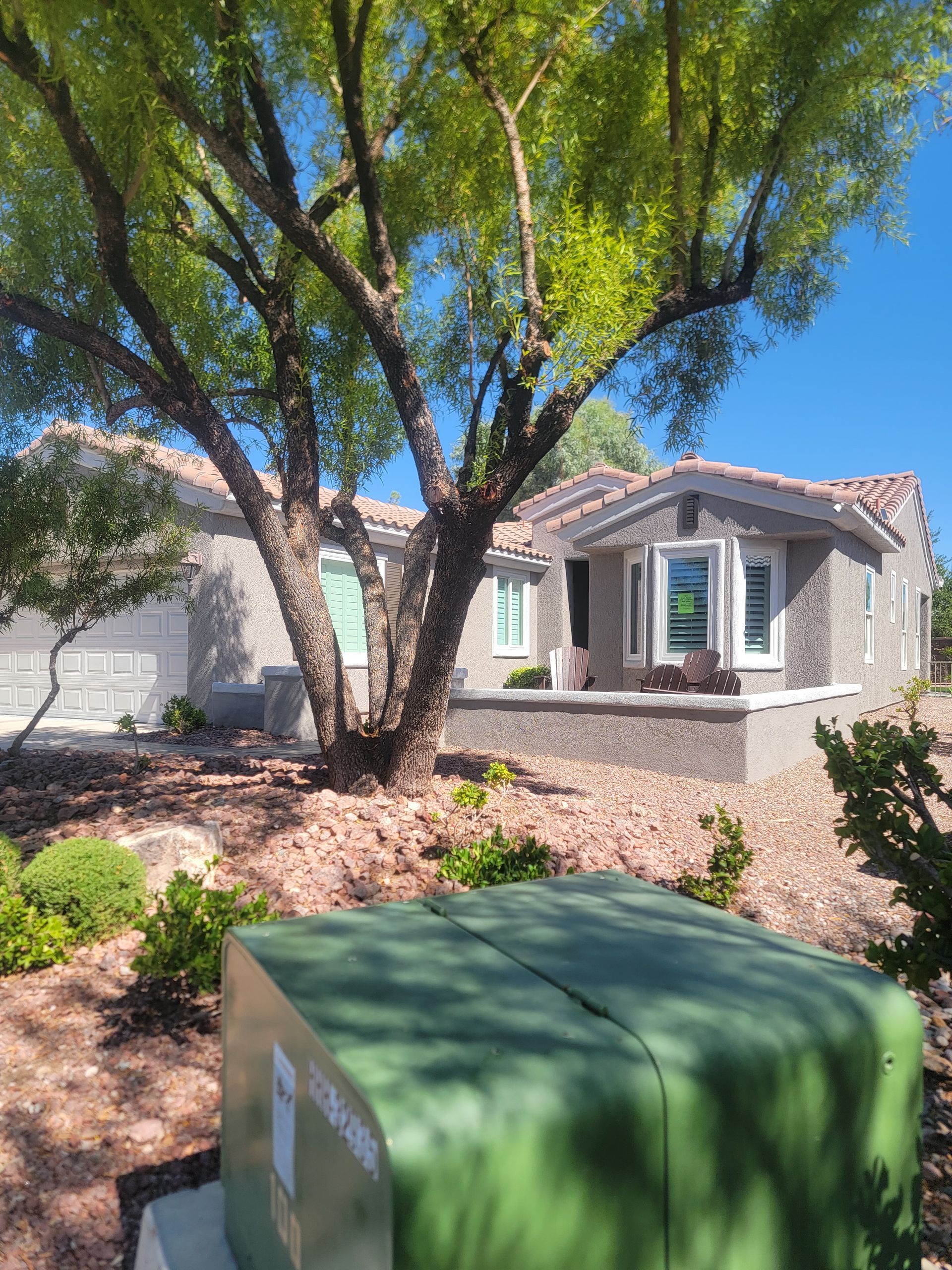 Green electrical box in front of a house with a tree.