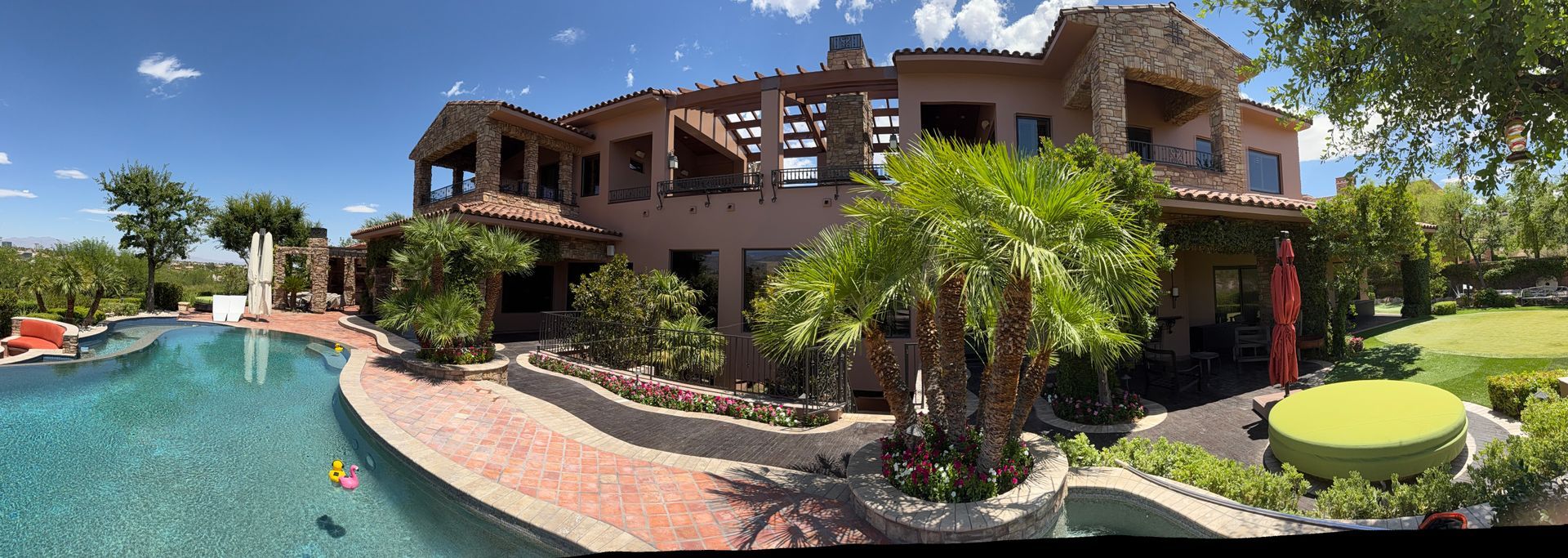 Large luxurious house with a pool, lush landscaping, and clear blue sky.