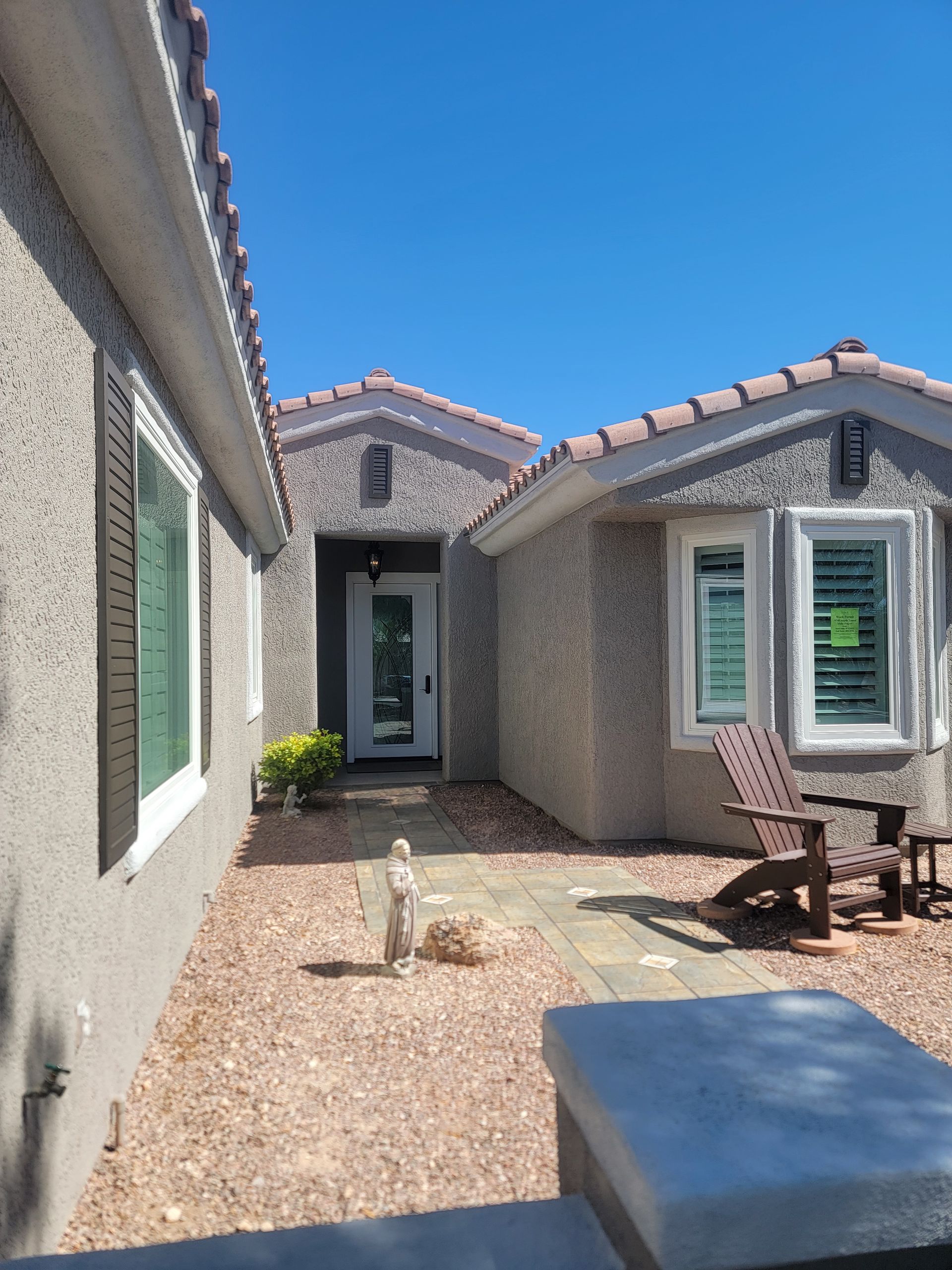 Exterior view of a stucco home with a pathway leading to the front door, blue sky overhead.