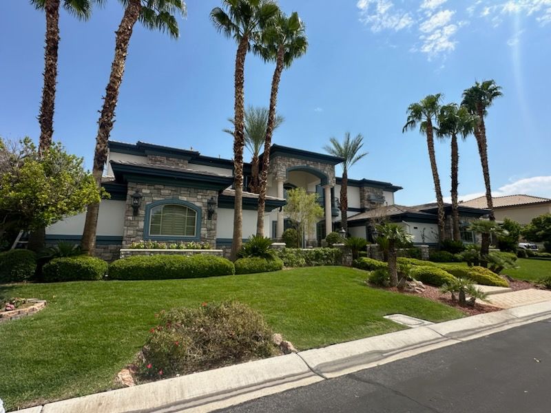 Luxurious house with stone facade, palm trees, and manicured lawn under a sunny sky.