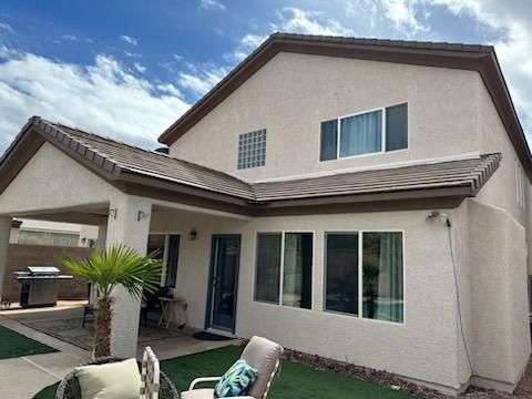 Beige two-story house with brown trim and roof, windows, patio, and a palm tree in the yard.