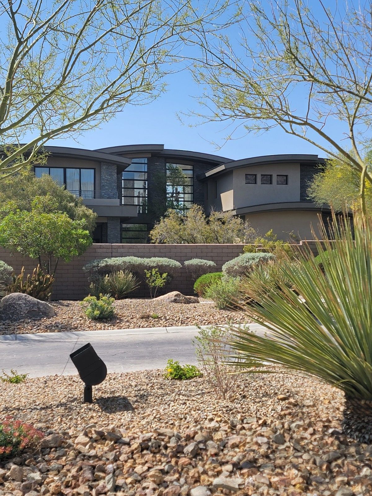 Modern house with large windows, surrounded by desert landscaping and blue sky.