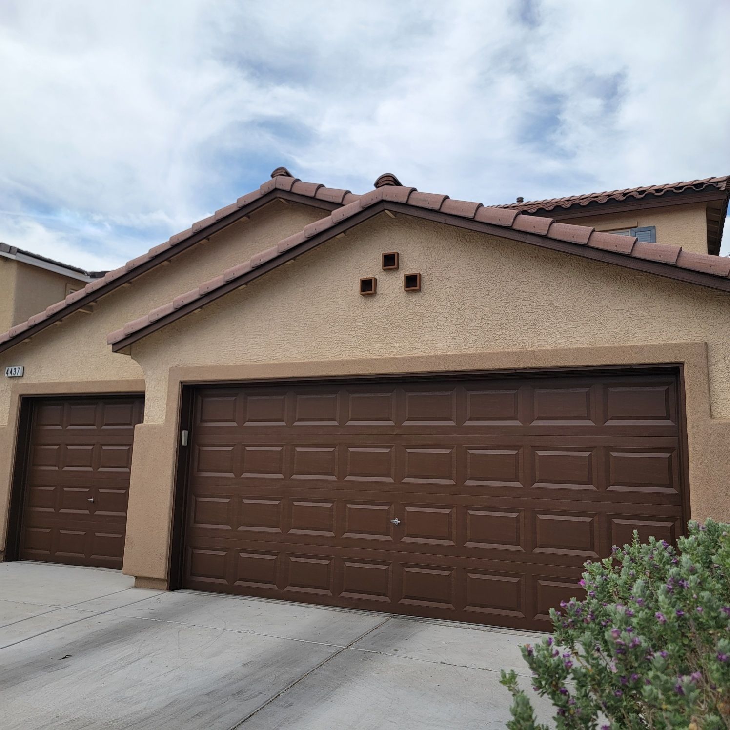 Brown two-car garage doors on a tan house with a clay tile roof.