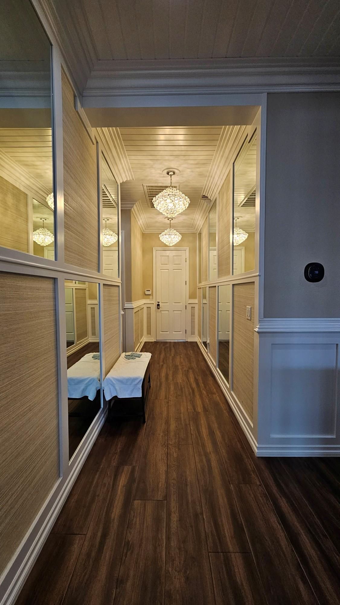 A hallway with hardwood floors , mirrors and a bench.