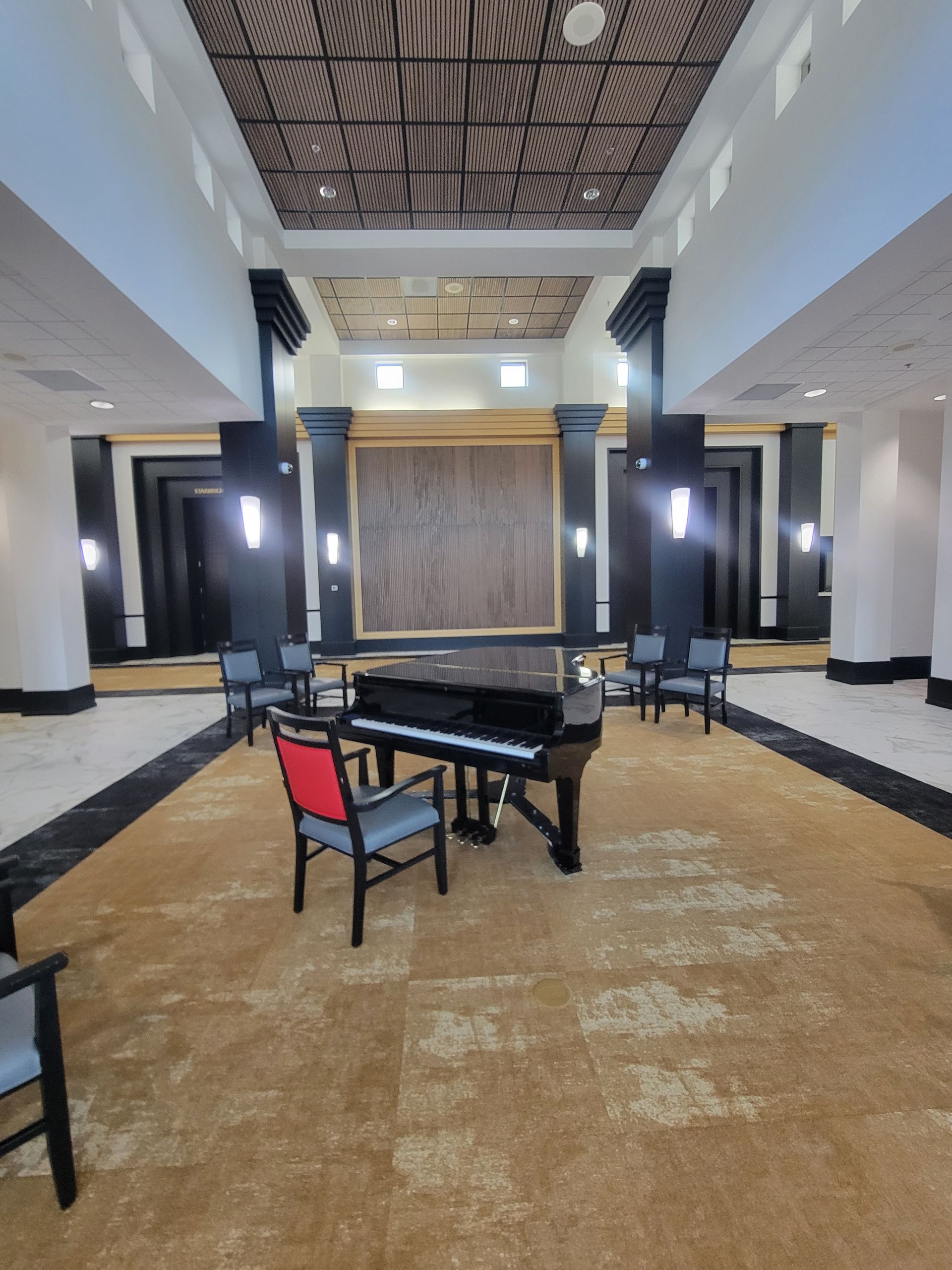 Grand piano on golden rug in a formal room, surrounded by chairs.