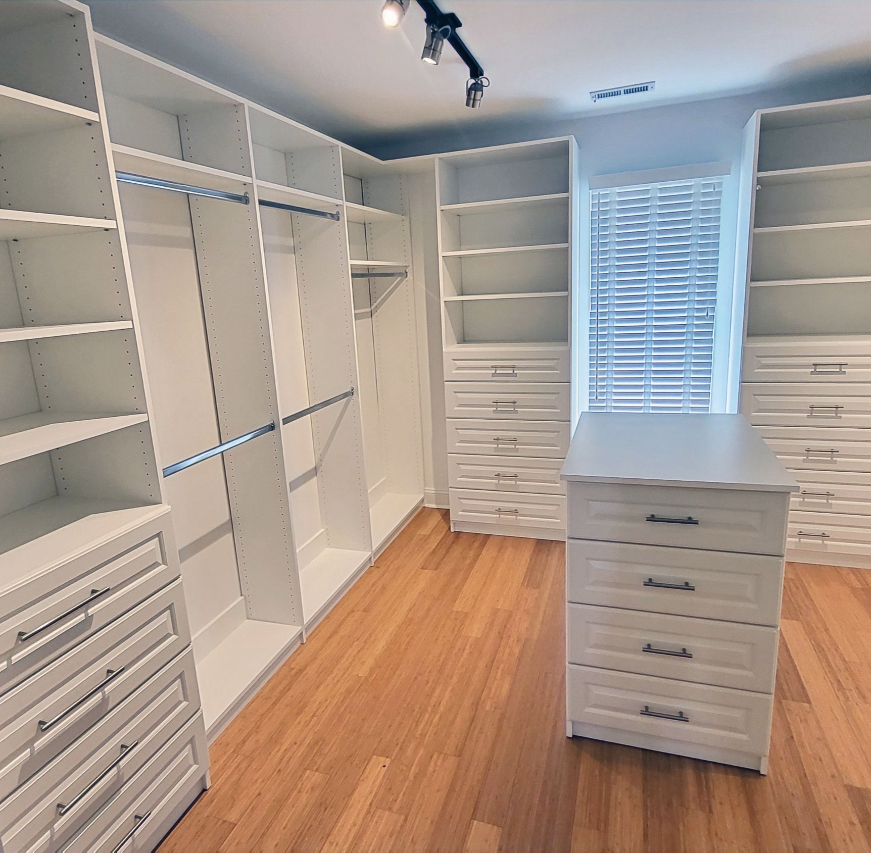 Empty white walk-in closet with shelves, drawers, and a center island, hardwood floor.