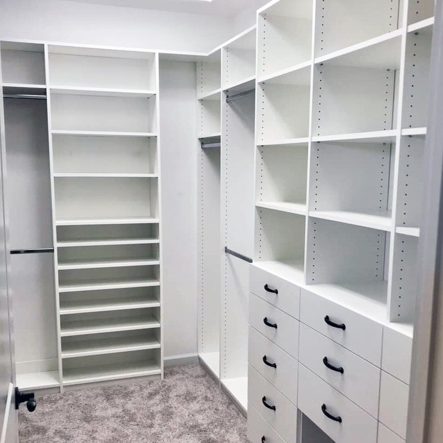 Walk-in closet with white shelving and drawers on a light carpet.