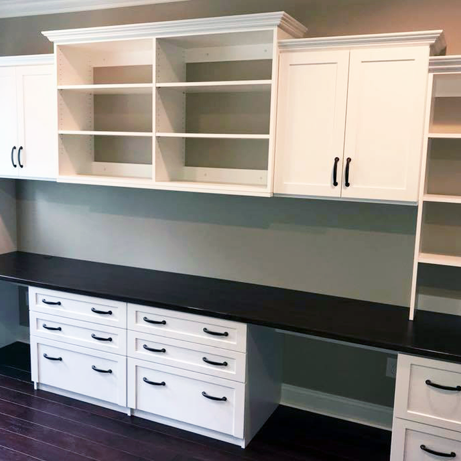 White built-in desk with black countertop and overhead cabinets. Dark wood floors.