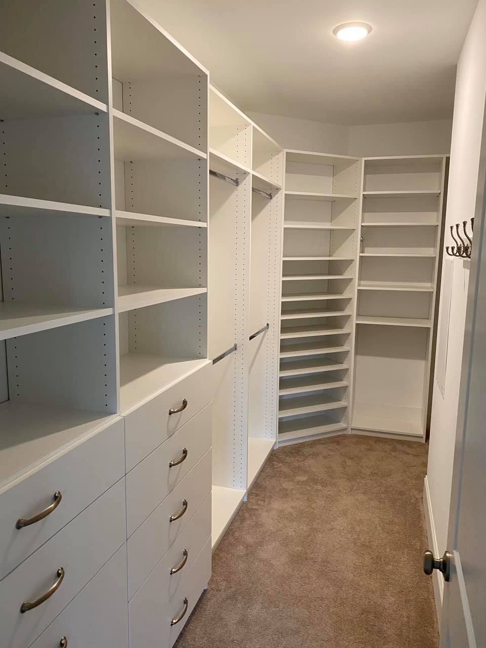 White, organized walk-in closet with shelves, drawers, and hanging rods; neutral-colored carpet.