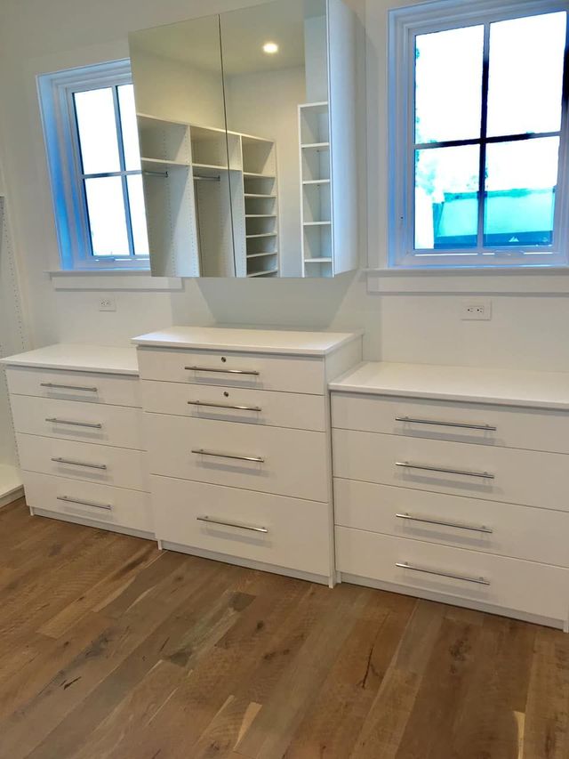 White dresser with chrome handles, mirror, closet, and windows in a room with hardwood floors.