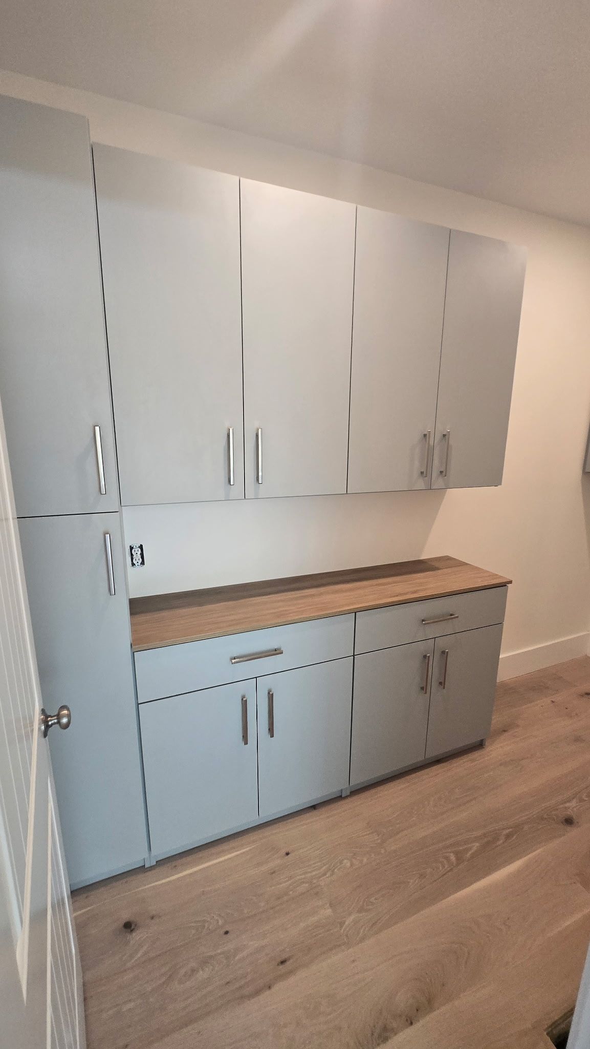 Built-in white cabinets with a wood countertop in a clean room with light wood flooring
