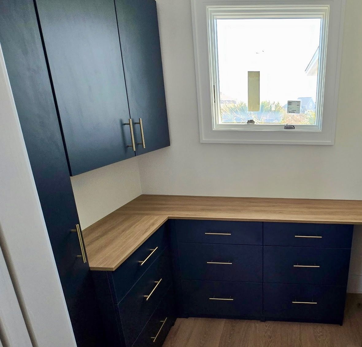 Small kitchen nook with navy cabinets, wood countertop, and a window above the corner sink area