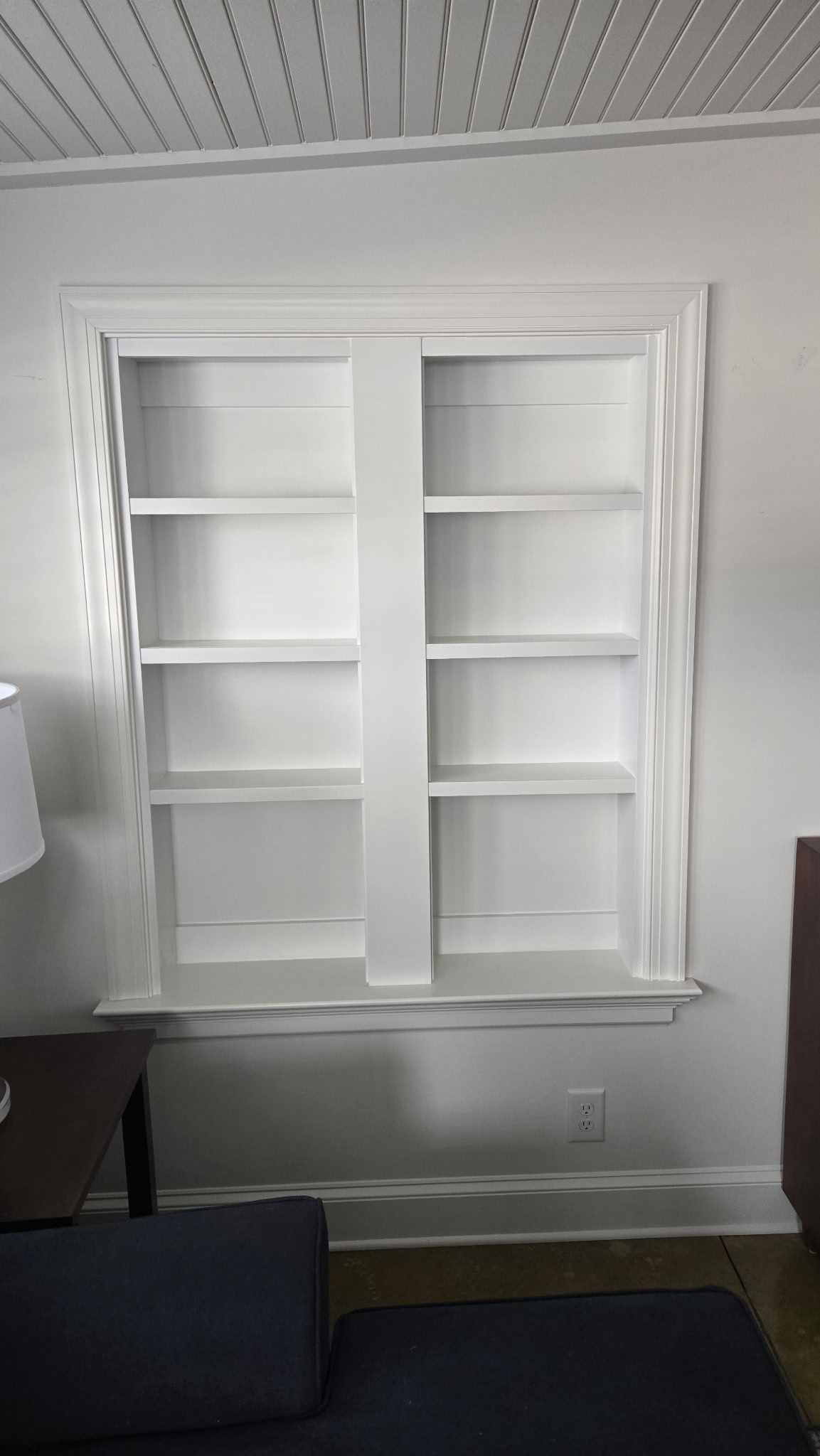 White built-in wall shelves in a small room with a window and a floor lamp on the left.