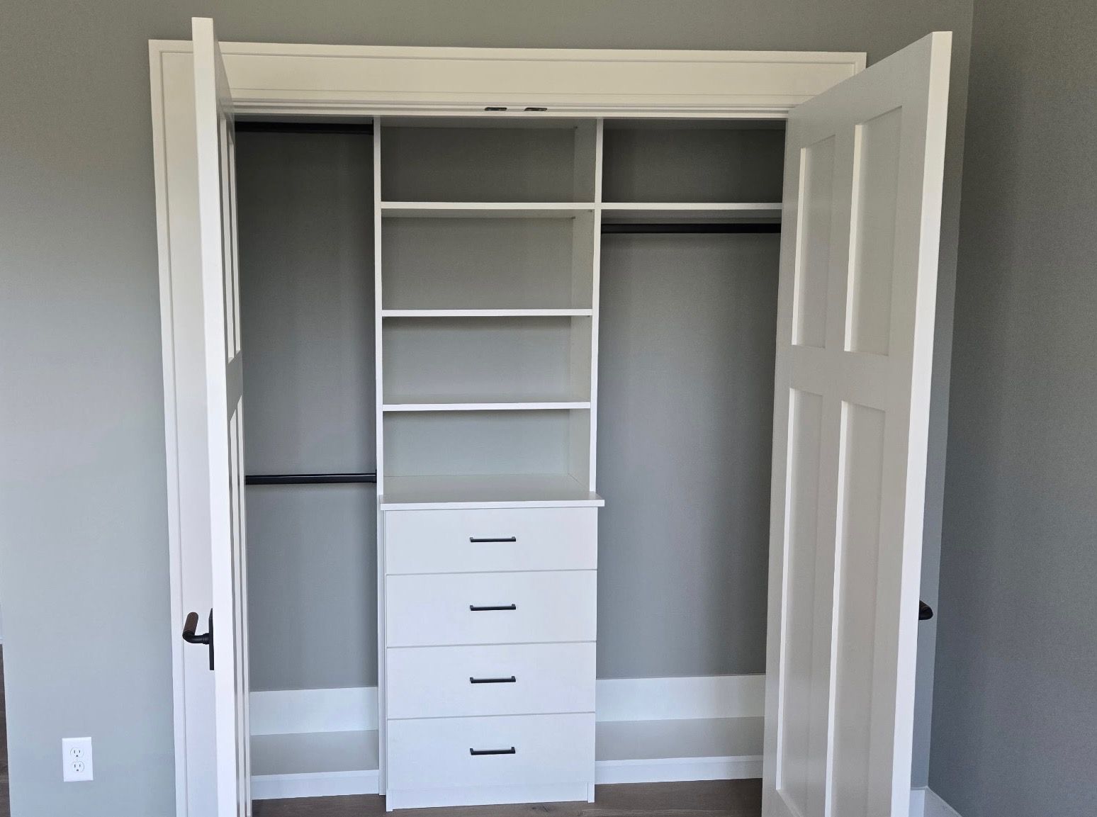Open closet with built-in shelves, drawers, hanging rods, and white double doors in a gray room