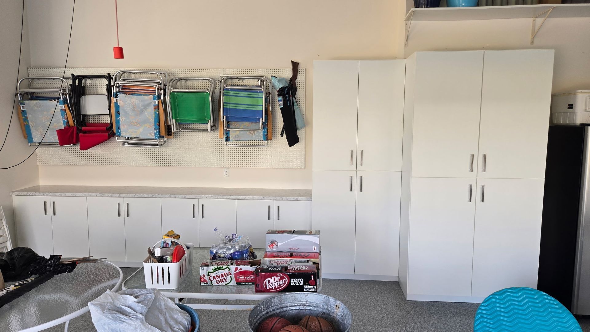 Garage wall with white cabinets and shelves holding colorful storage bins and supplies
